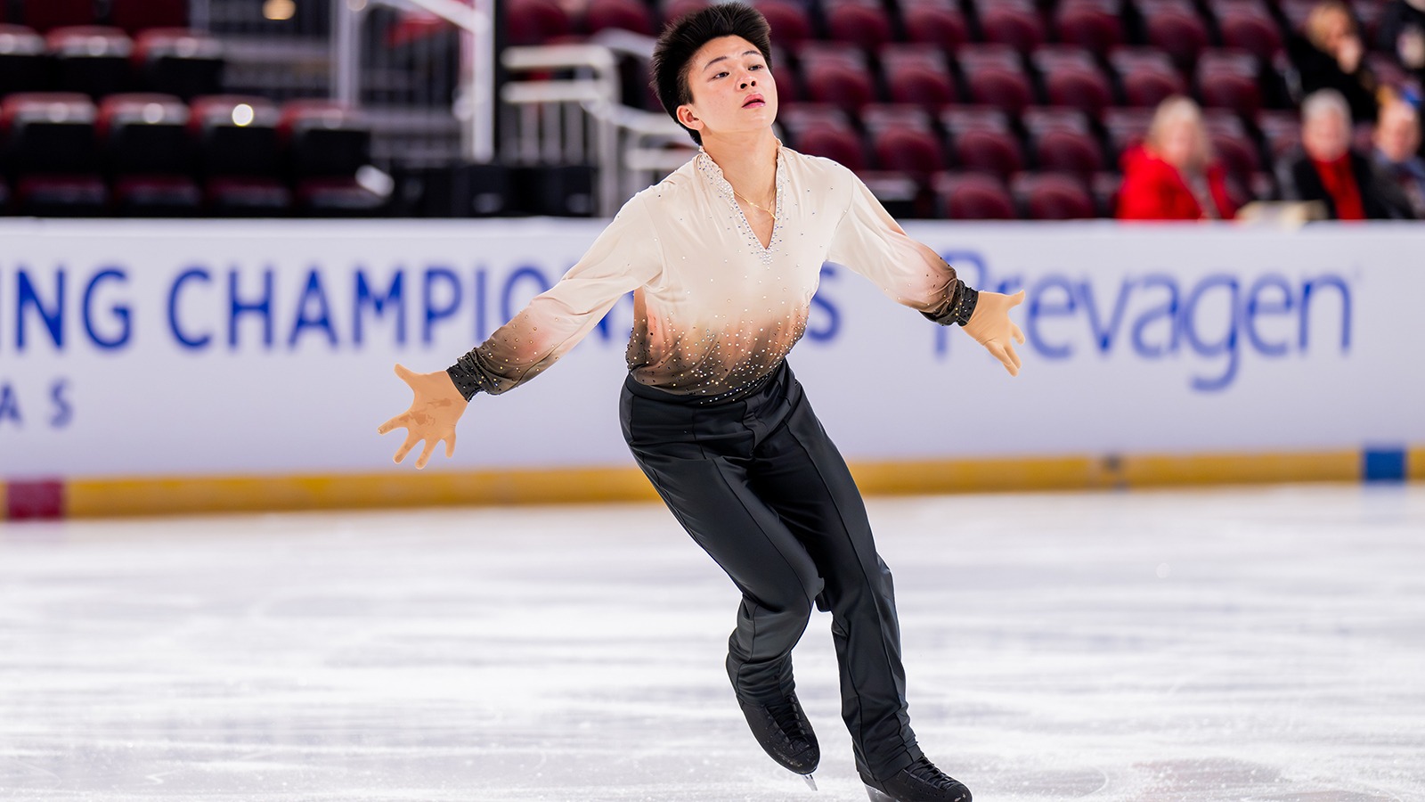 Lorenzo Elano, arms extended, with palms up, performs at the 2025 U.S. Championships in Wichita, Kansas. He's wearing black pants and a shirt that's white with brown and black highlights around the bottom of the torso.