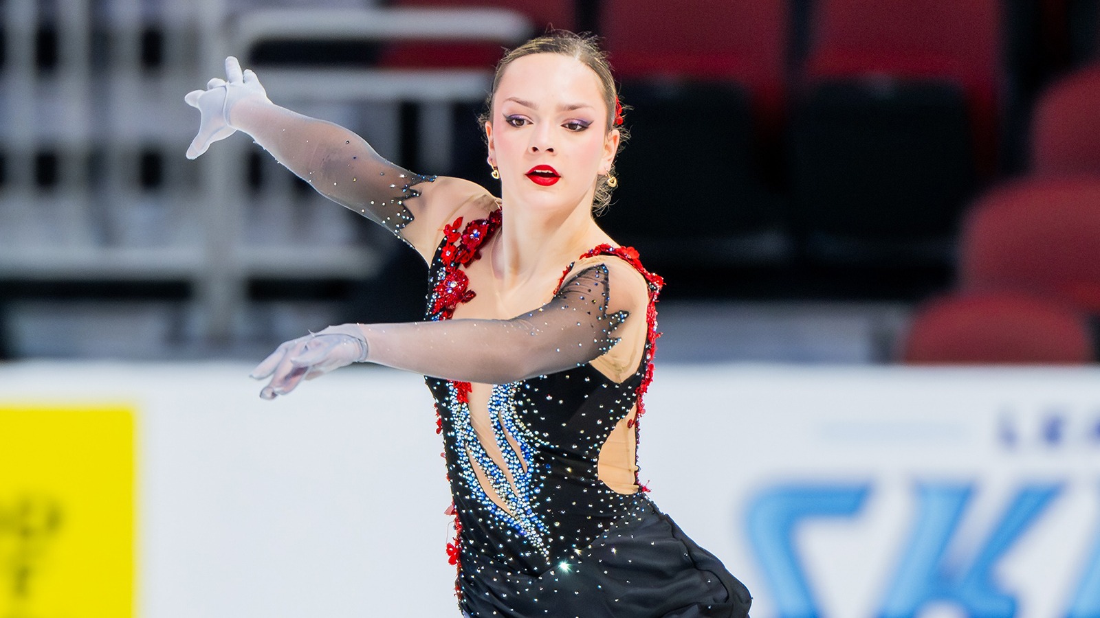 Wearing red, with sheer sleeves and gloves, Emilia Nemirovsky performs on the ice.