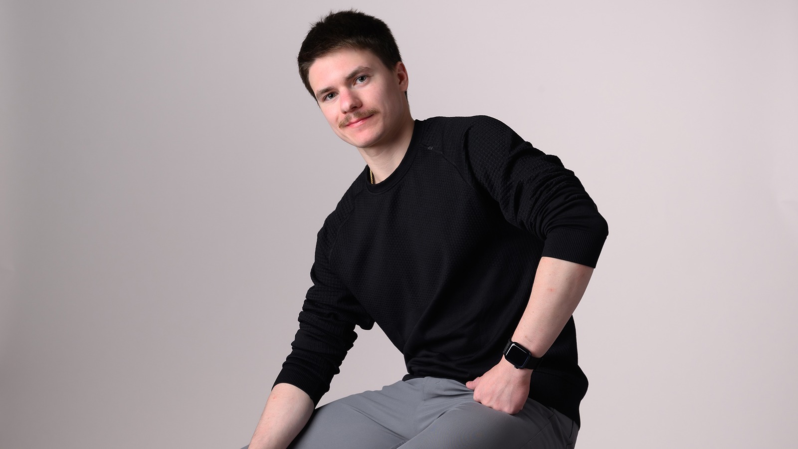 Max Naumov, dressed in a black shirt and gray pants, sits on a stool for a photo shoot at Champs Camp.
