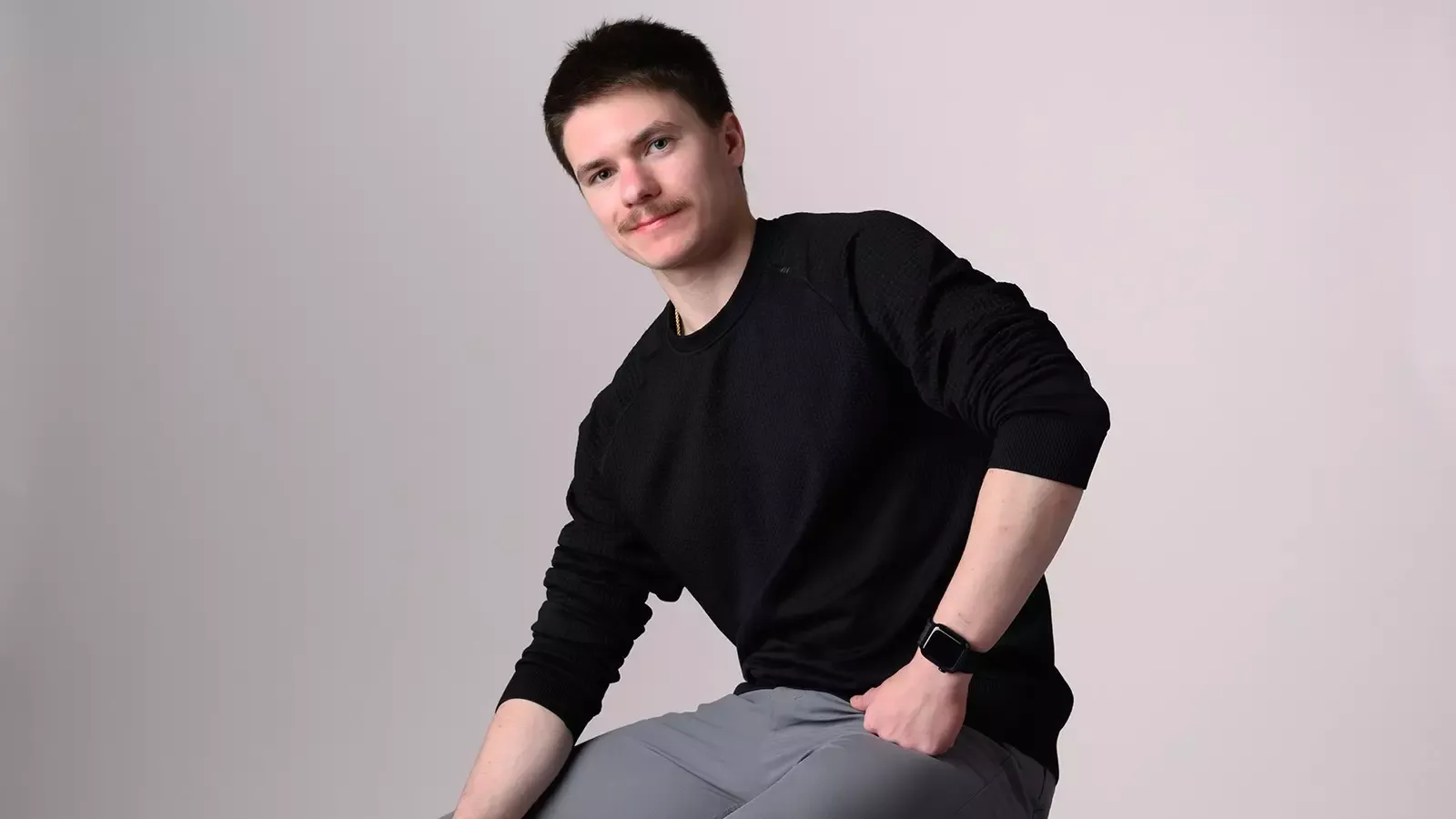 Max Naumov, dressed in a black shirt and gray pants, sits on a stool for a photo shoot at Champs Camp.