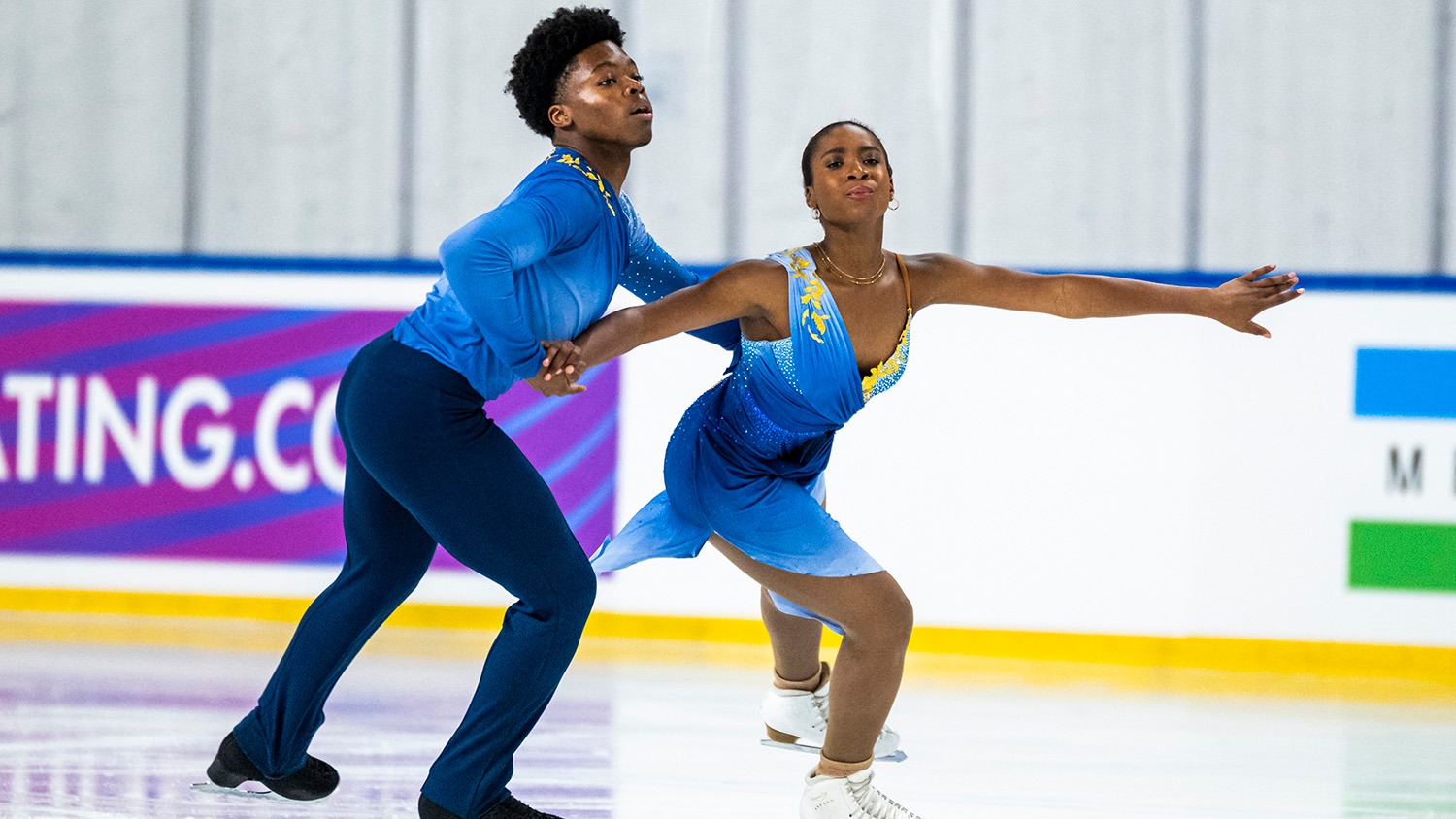 Anaelle Kouevi and Yann Homawoo skate in hold at JGP Turkey. She wears an ombre blue dress with yellow detail on teh shoulders while he wears a blue top of the same color and navy pants.
