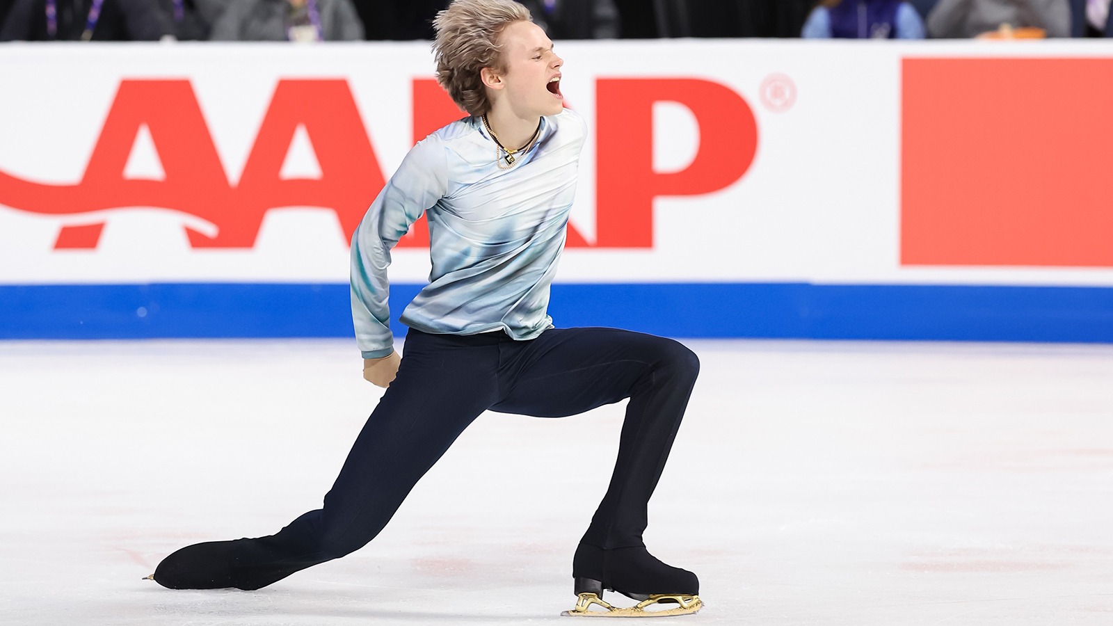 Wearing a white, long-sleeve shirt and black pants, Ilia Malinin shows his emotion during a program at Skate America.