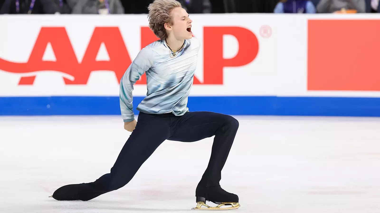 Wearing a white, long-sleeve shirt and black pants, Ilia Malinin shows emotion during a performance at Skate America.