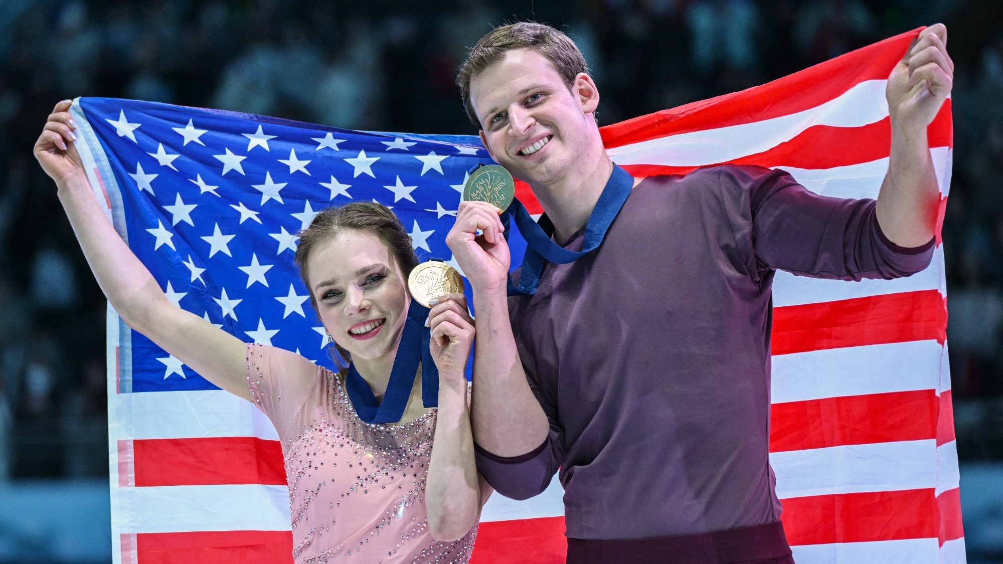 Alisa Efimova and Misha Mitrofanov wear their gold medals and hold up the American flag at the Four Continents Championships.