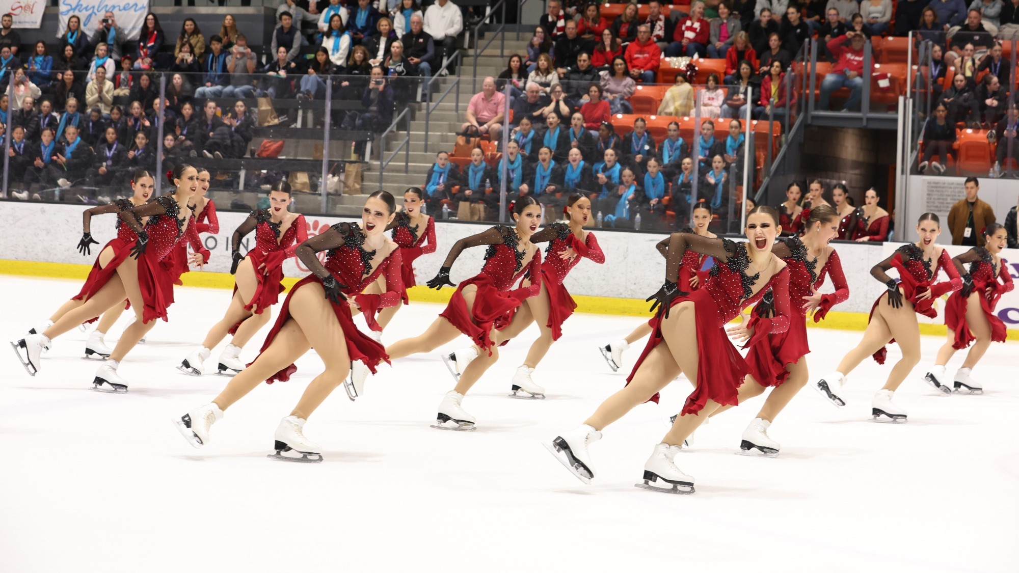Teams Elite junior synchro team skates in unison wearing coordinating red long sleeve skating costumes