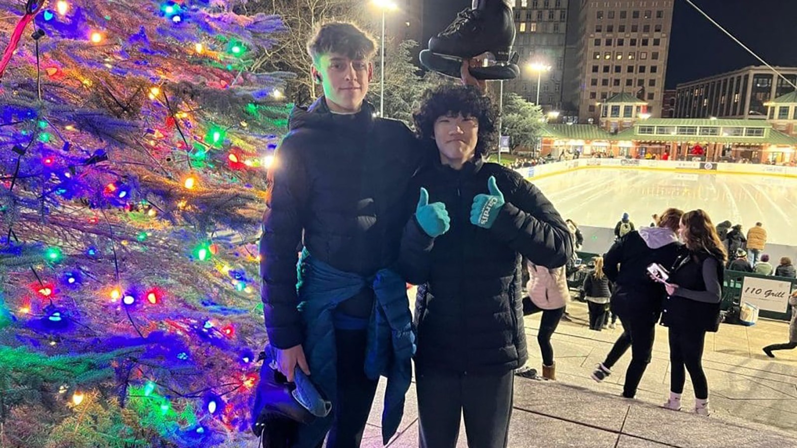 Patrick Blackwell and Spencer Lane stand in front of an outdoor rink during a holiday ice show. 