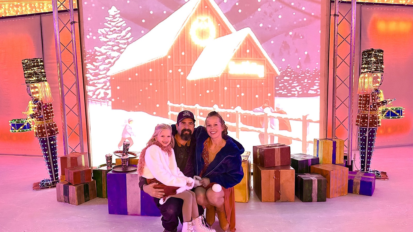 The Irvine family, Scott, Natalia Zaitseva, and their daughter, Sasha, in front of a winter wonderland landscape that has a red barn.