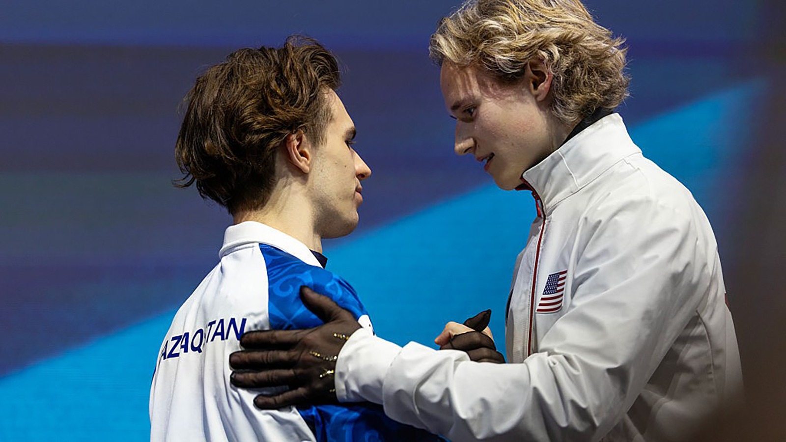 Ilia Malinin, dressed in his white Team USA jacket, congratulates Kazakhstan's Mikhail Shaidorov for winning the Olympic gold medal.