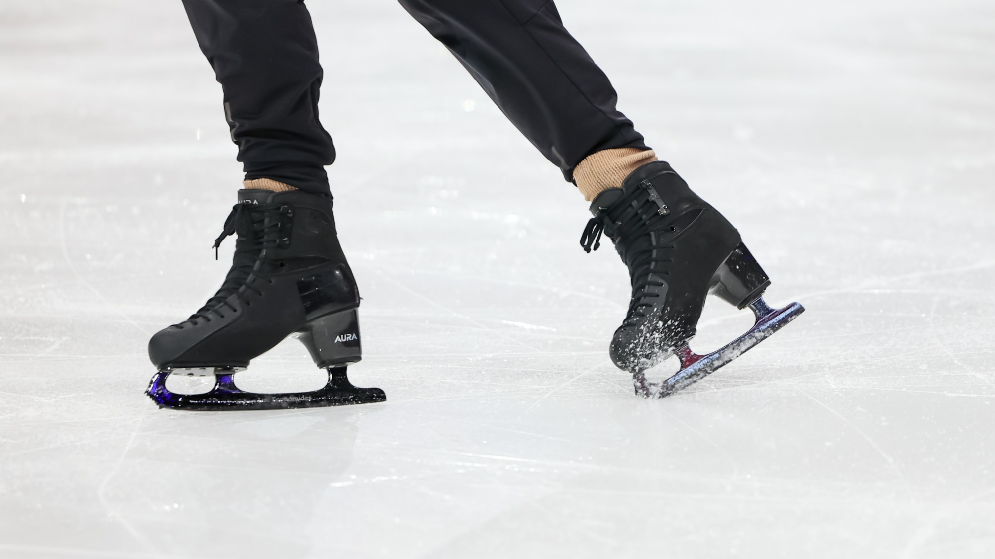 Closeup of a pair of black skates. The skater is wearing black pants