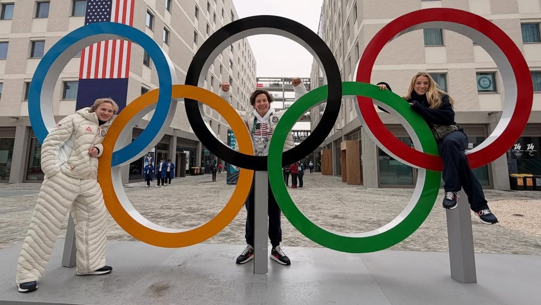 Ilia Malinin, Vadym Kolesnik and Emilea Zingas stand in front of the Olympic rings in the Olympic village at the 2026 Olympic Winter Games in Milan