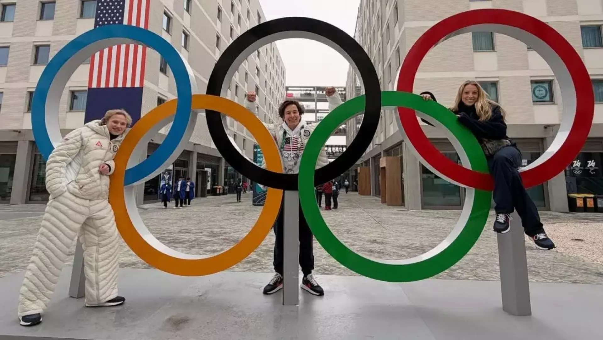 Ilia Malinin, Vadym Kolesnik and Emilea Zingas stand in front of the Olympic rings in the Olympic village at the 2026 Olympic Winter Games in Milan