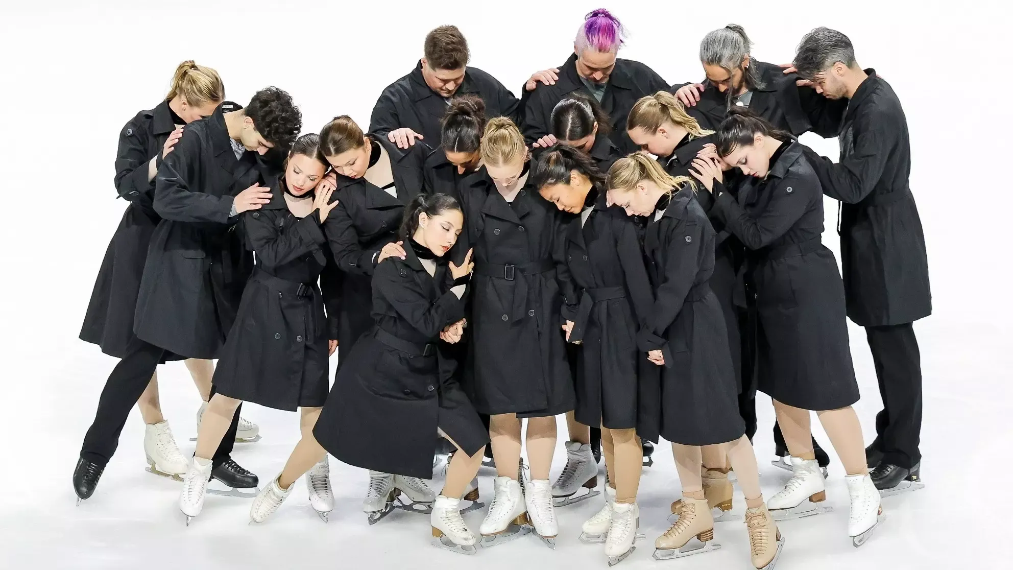 Forte of Boston, The Skating Club of Boston's senior Theatre On Ice Team, stands together as a group wearing matching black trench coats and leaning on each other for support after performing an emotional program. 