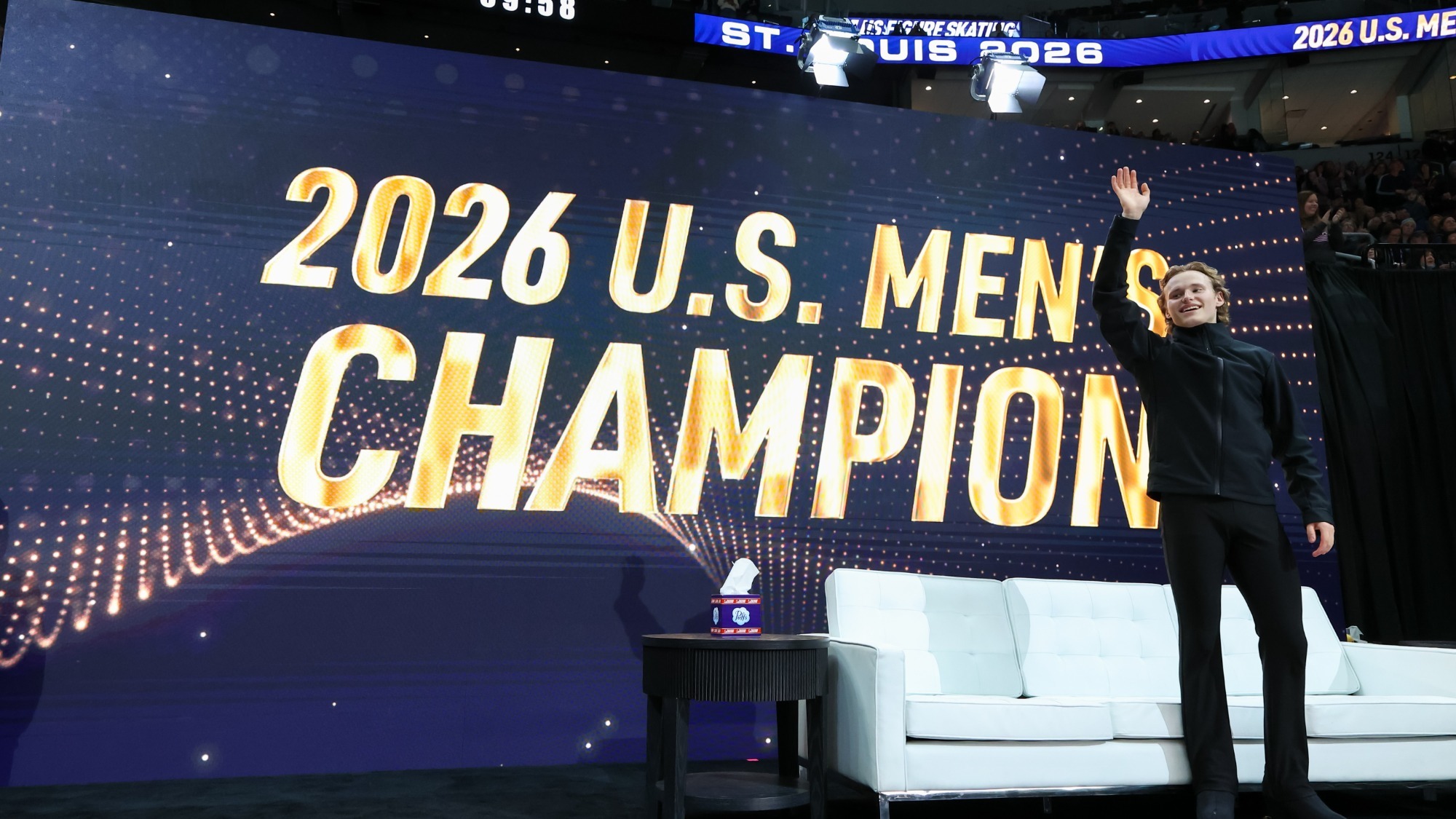 Ilia Malinin waves to the fans, with a neon sign behind him: 2026 U.S. Men's Champion