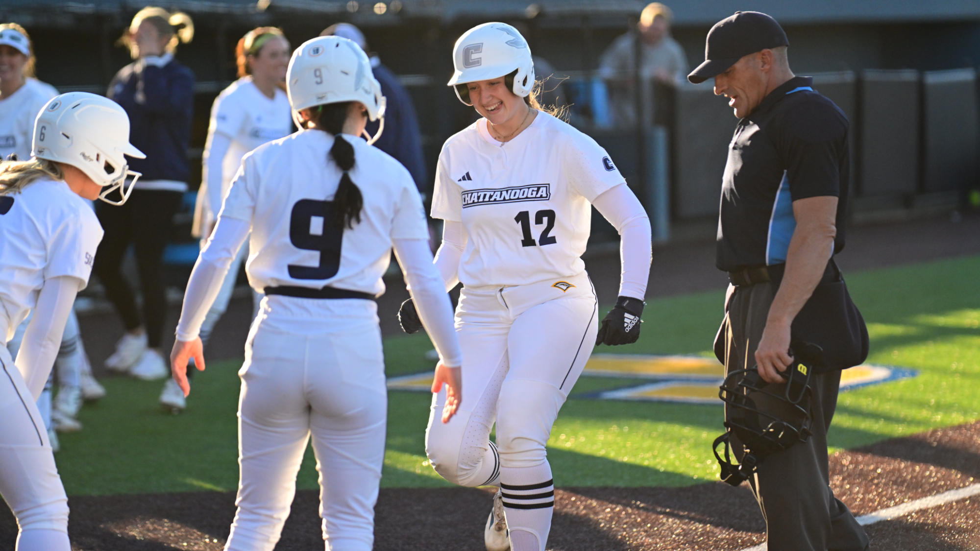 softball player tags home after hitting a home run and is greeted by her teammates while the umpire looks on.