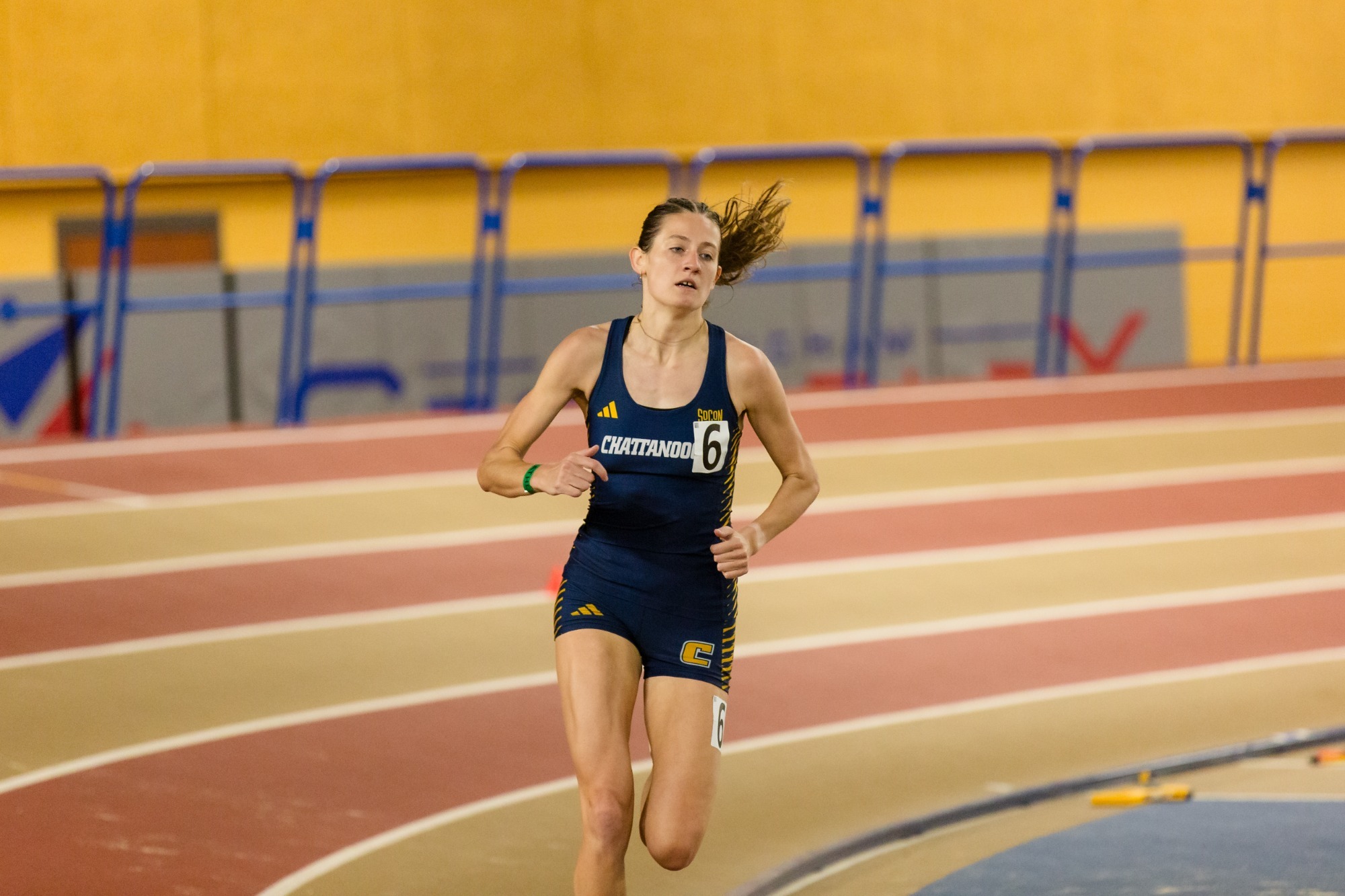 A female college athlete running on an indoor track.