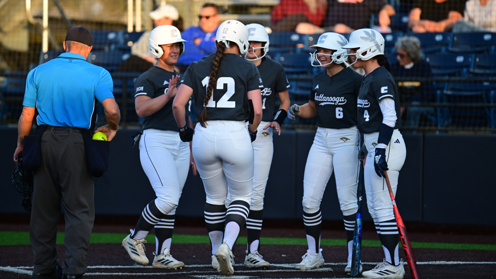 A softball runner is greeted at home plate by her teammates after hitting a three-run home run.