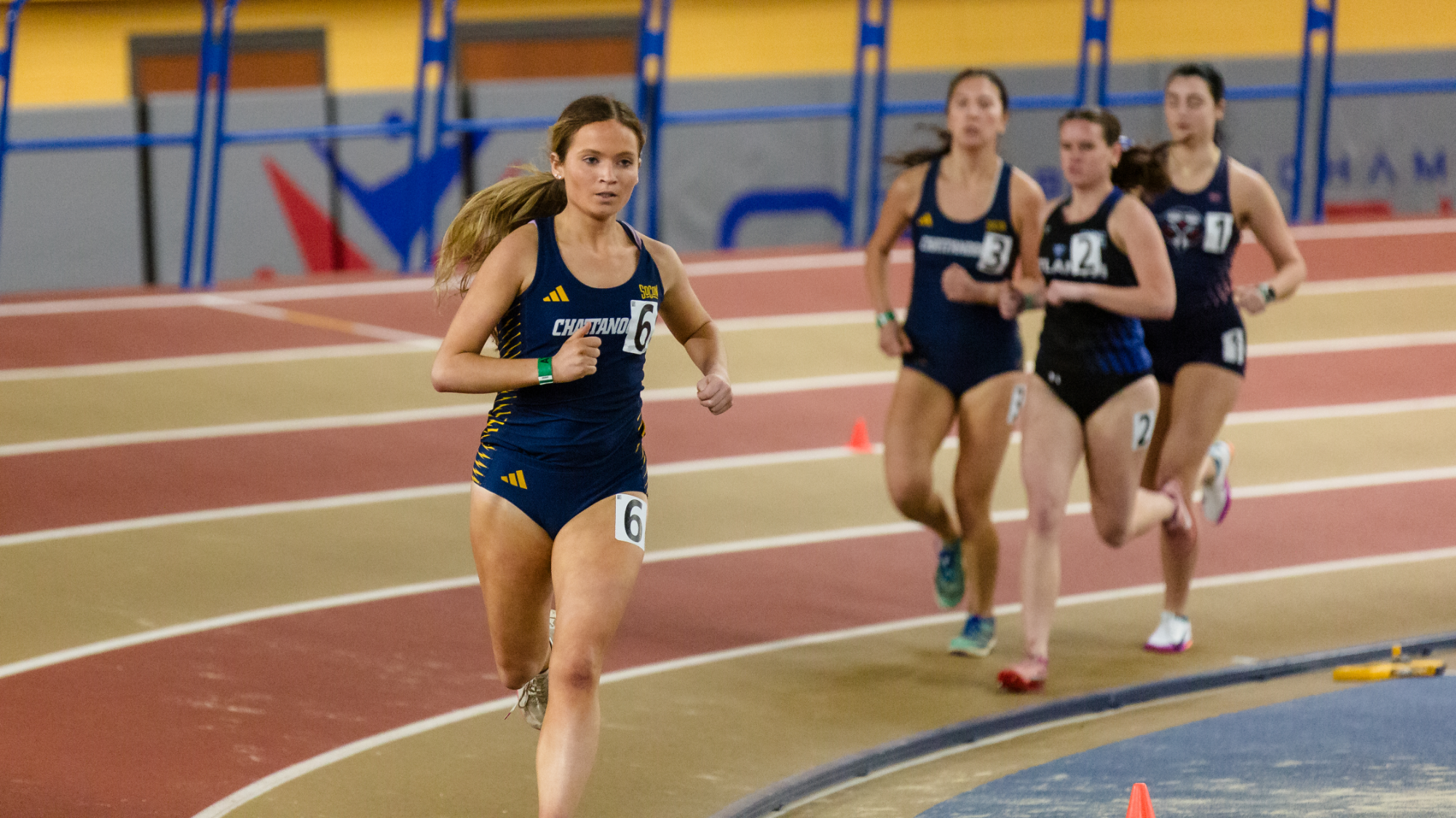 Women running around an indoor track at a Division I track meet.