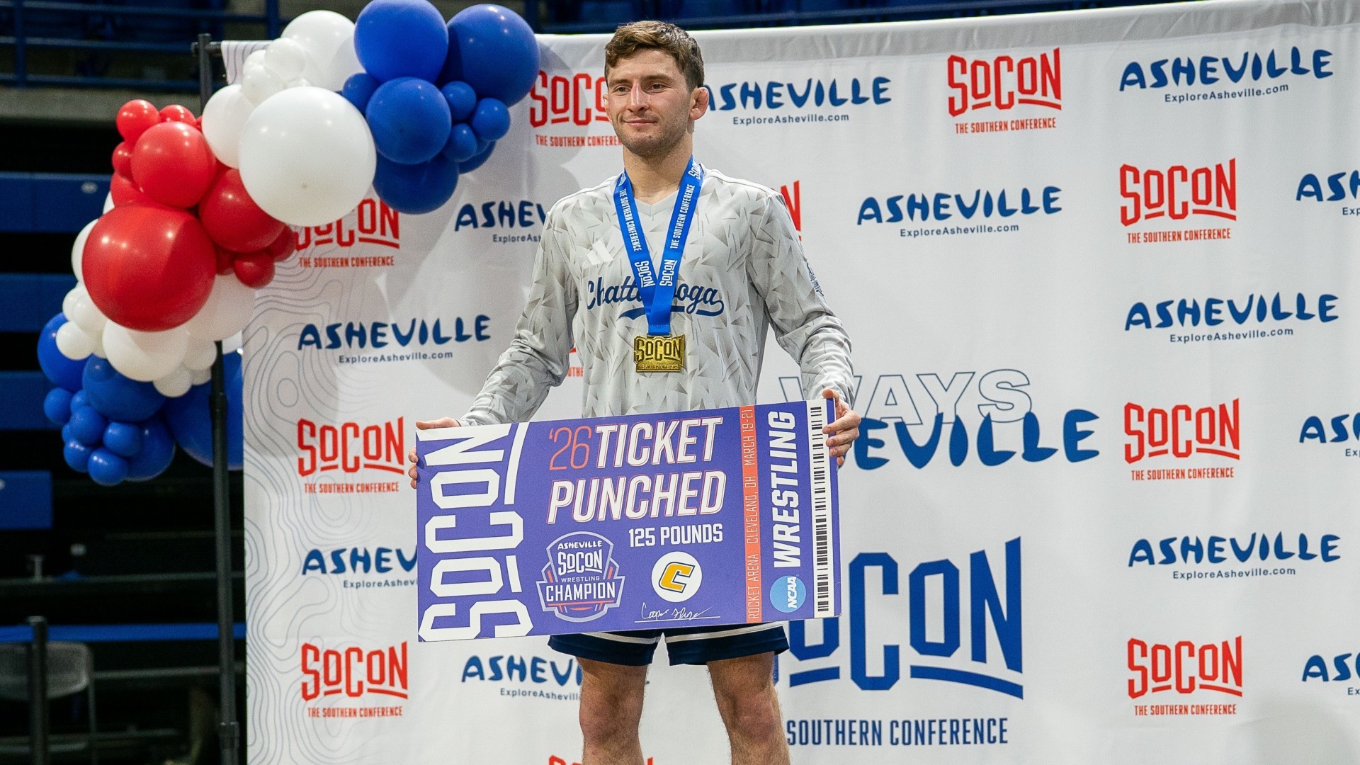 Cooper Flynn stands atop the SoCon podium holding his ticket poster that he punched to the 2026 NCAA Wrestling Championships 