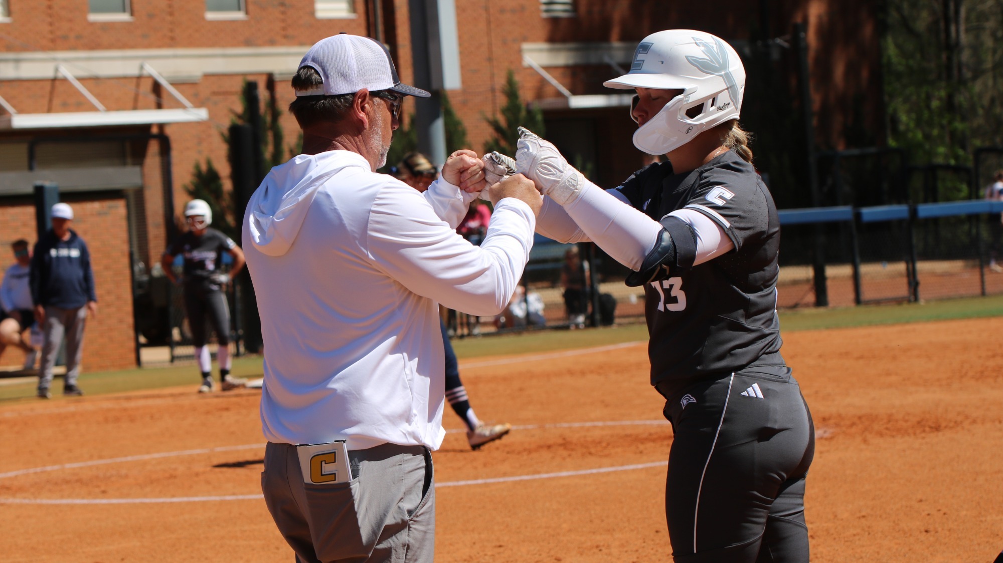 A softball player reaches first base and fists bumps with first base coach.
