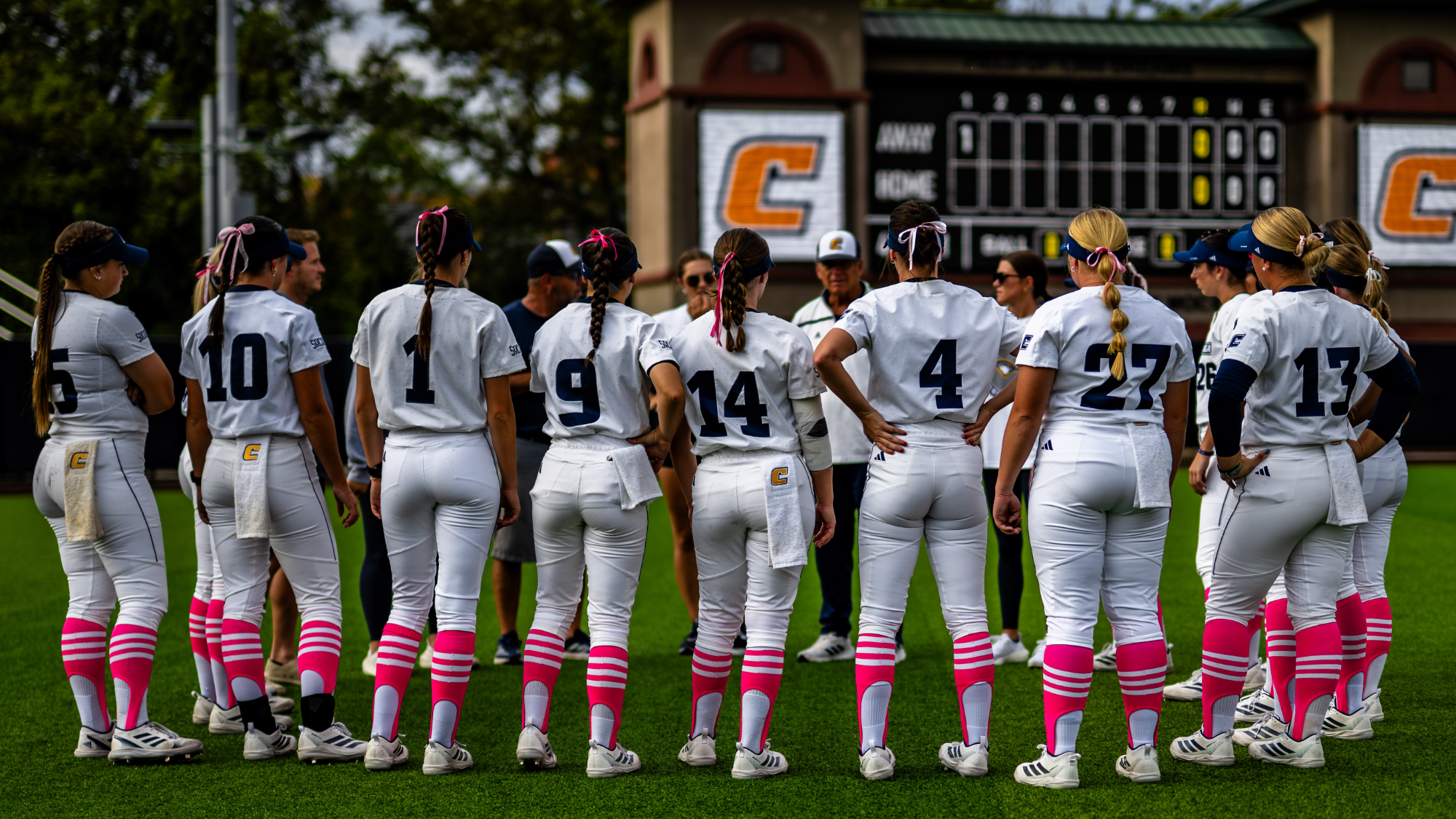 Softball Team wearing all white with pink socks in a huddle with the coach.