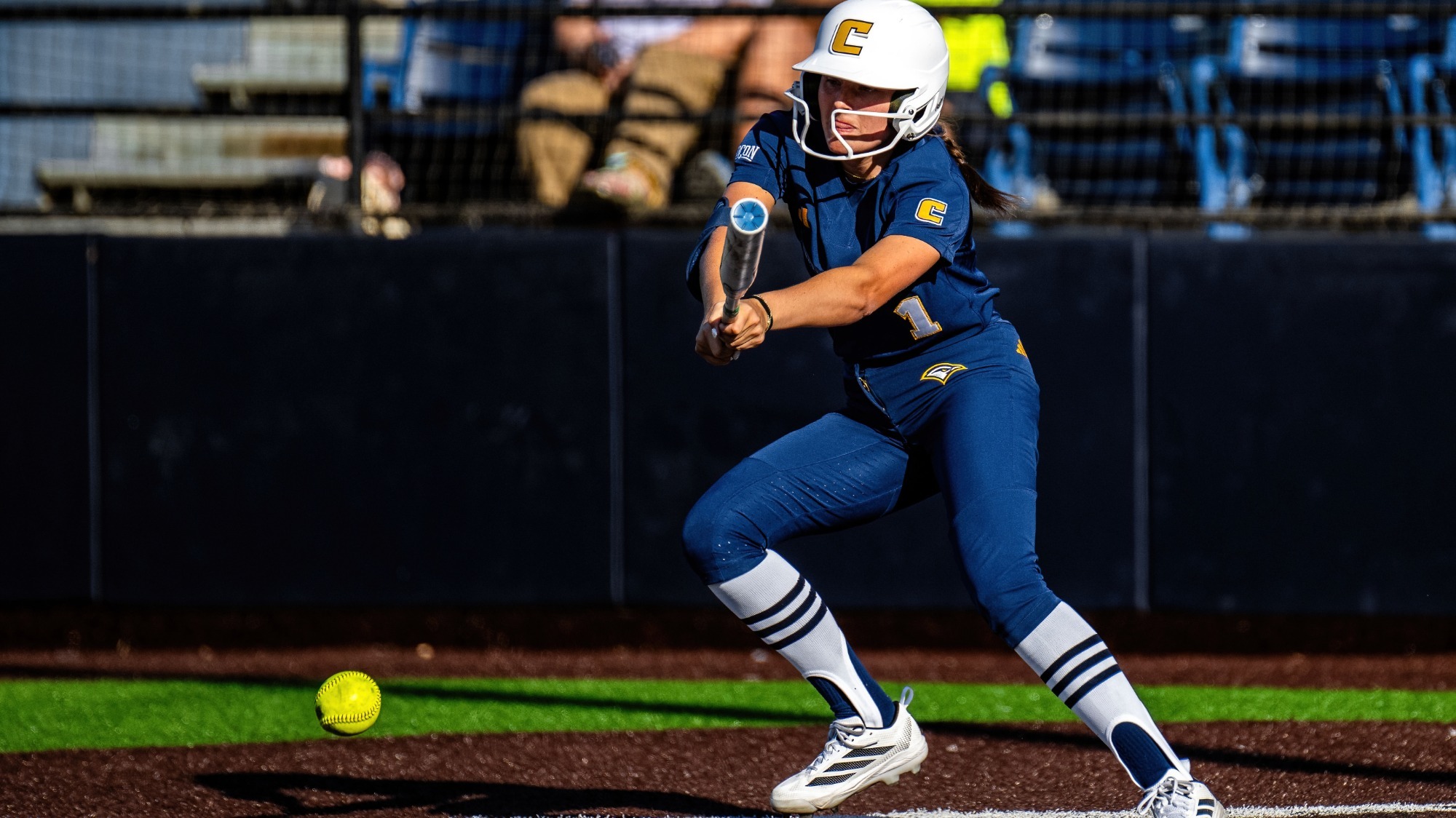 A left-handed softball player makes contact with the ball at the plate.