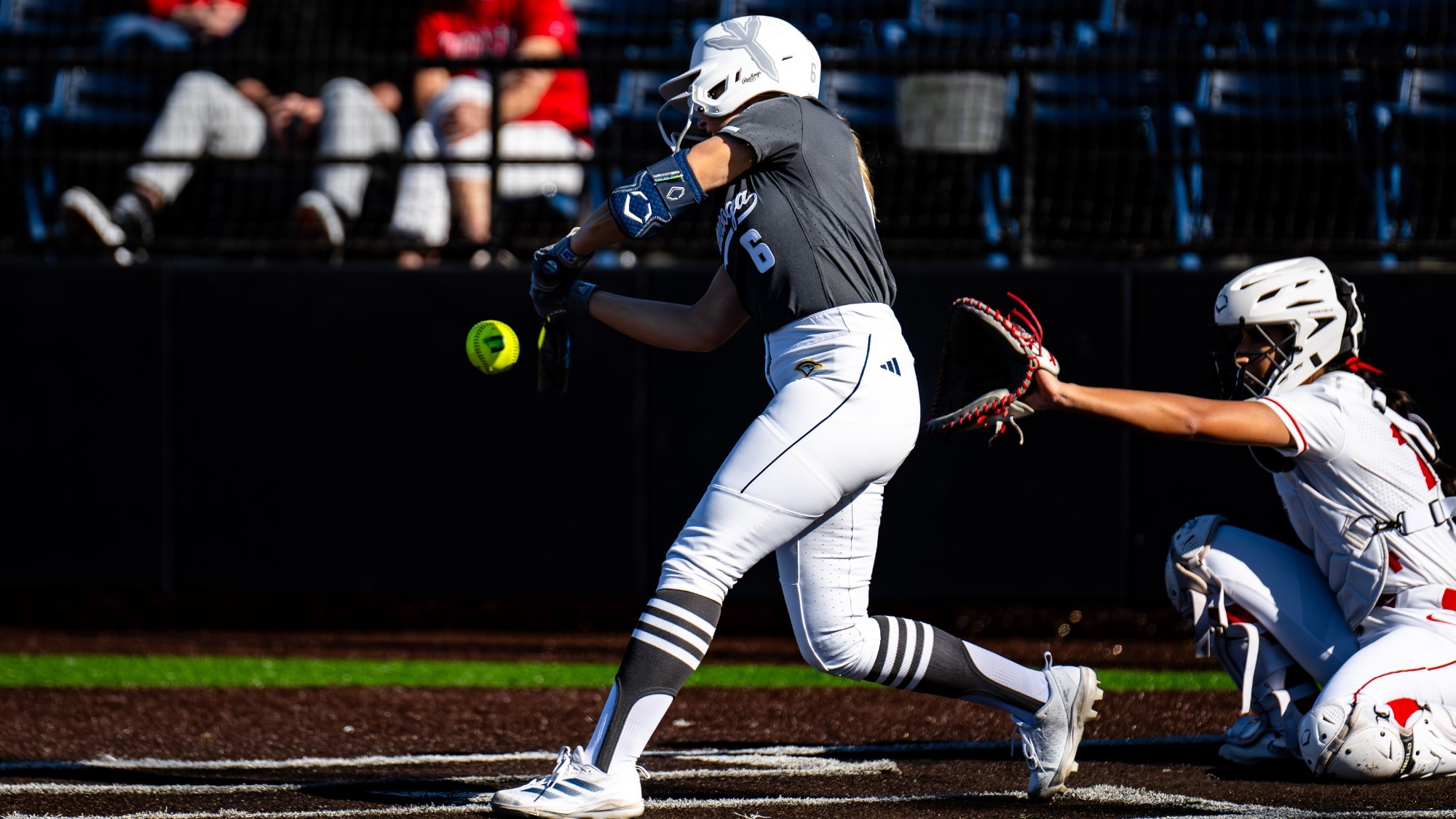 A softball player is at the plate and hitting the ball in a game