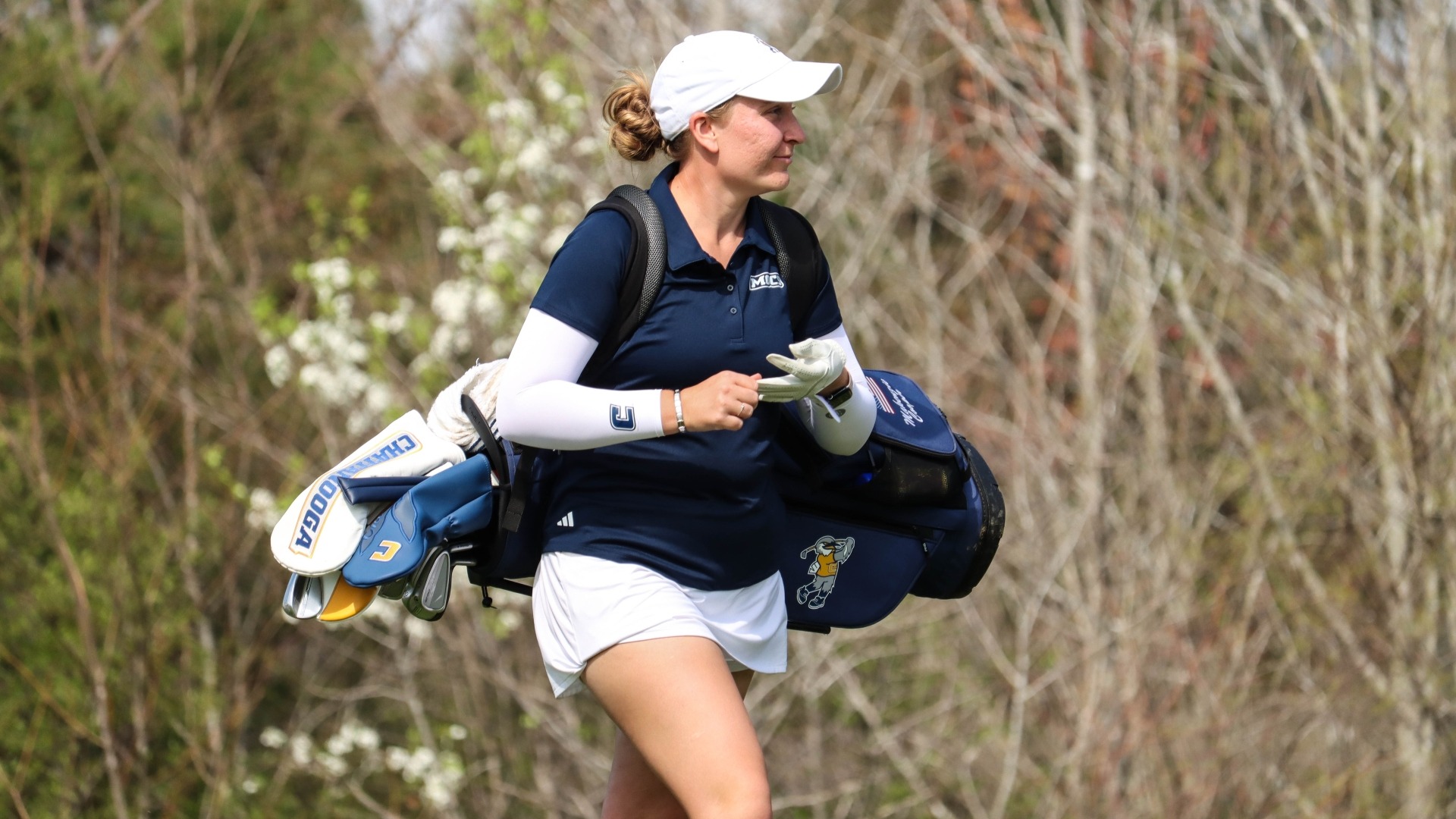 Makenzie Cooper walks towards the green with her bag and starts to take off her glove in preparation for a birdie putt