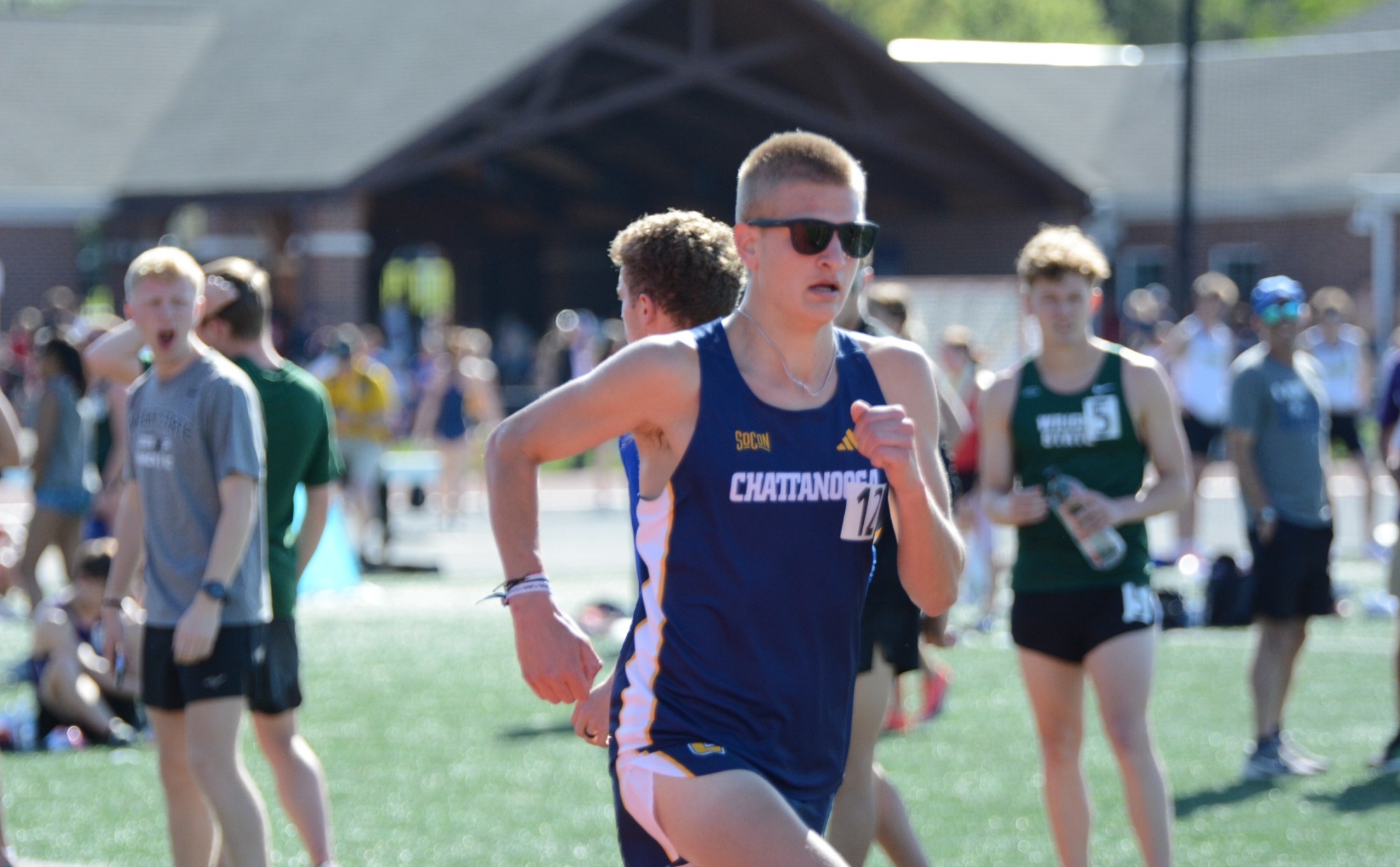 A male college athlete is running a race on a track on a sunny day.