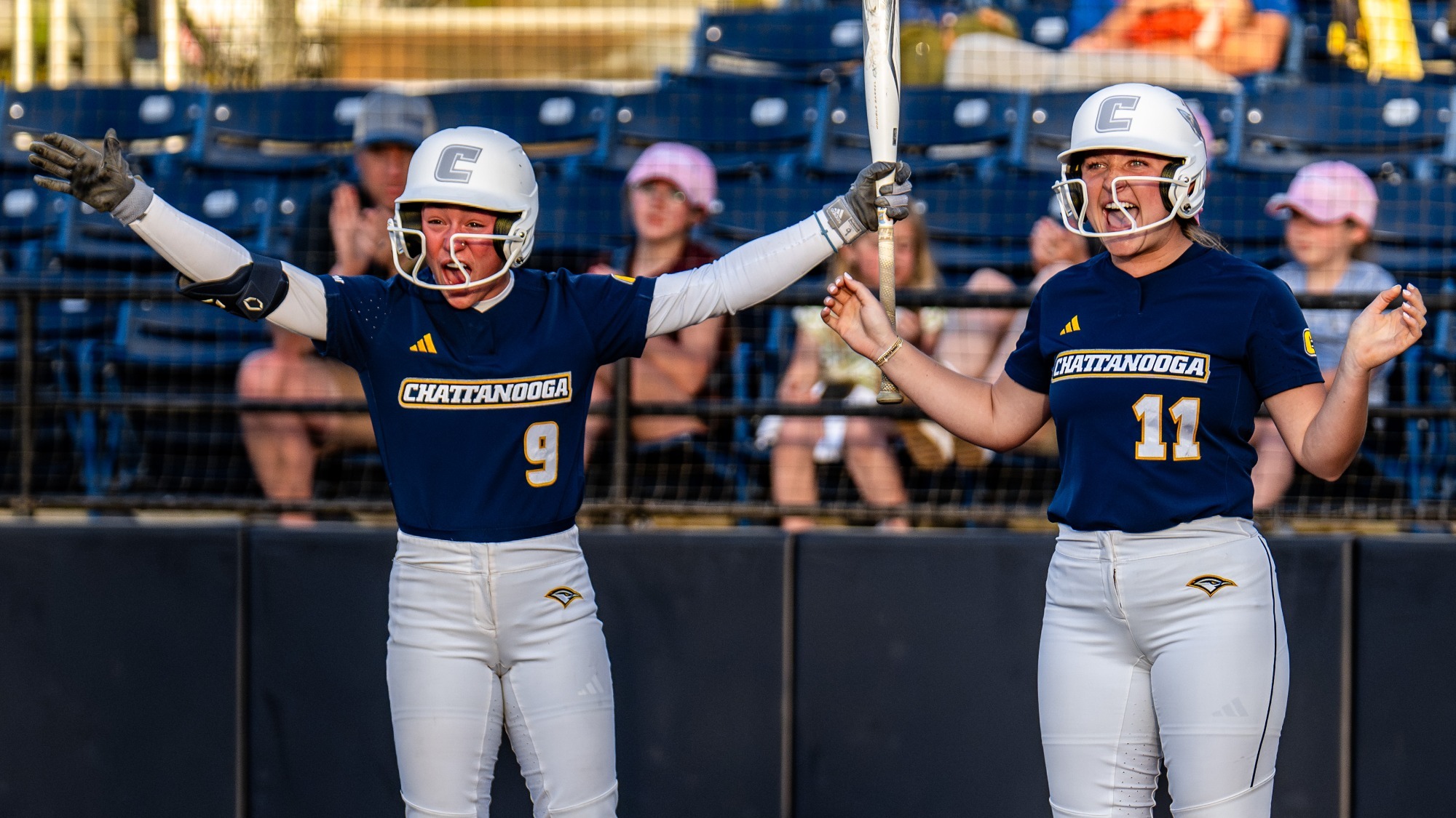 Two softball players are celebrating with their arms out after their teammate hit a game winning double.