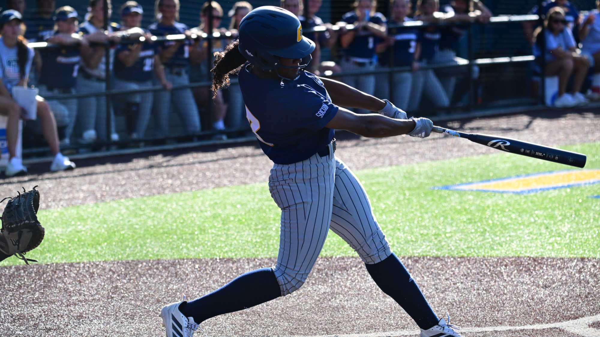 A softball player makes contact with the ball on a sunny day on the diamond.