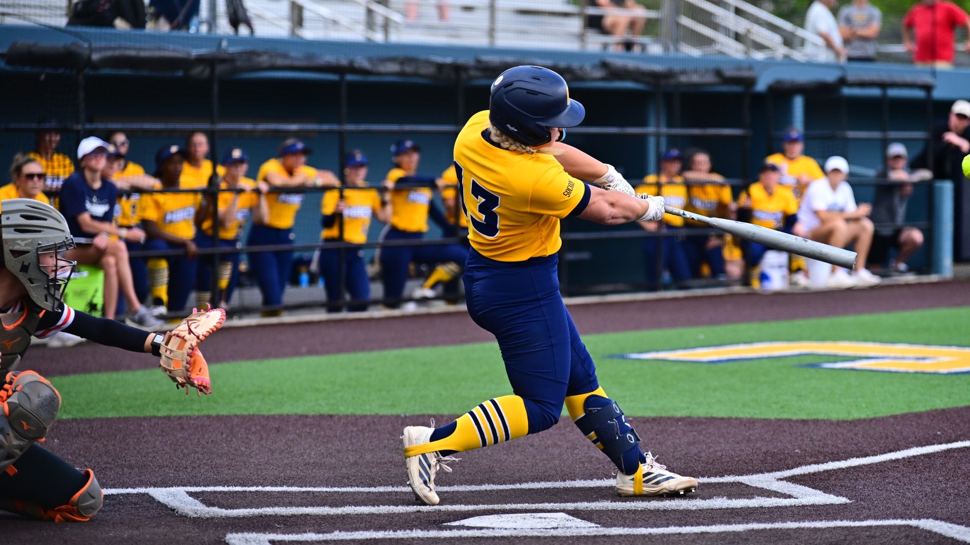 A softball player is at the plate and hits the ball.