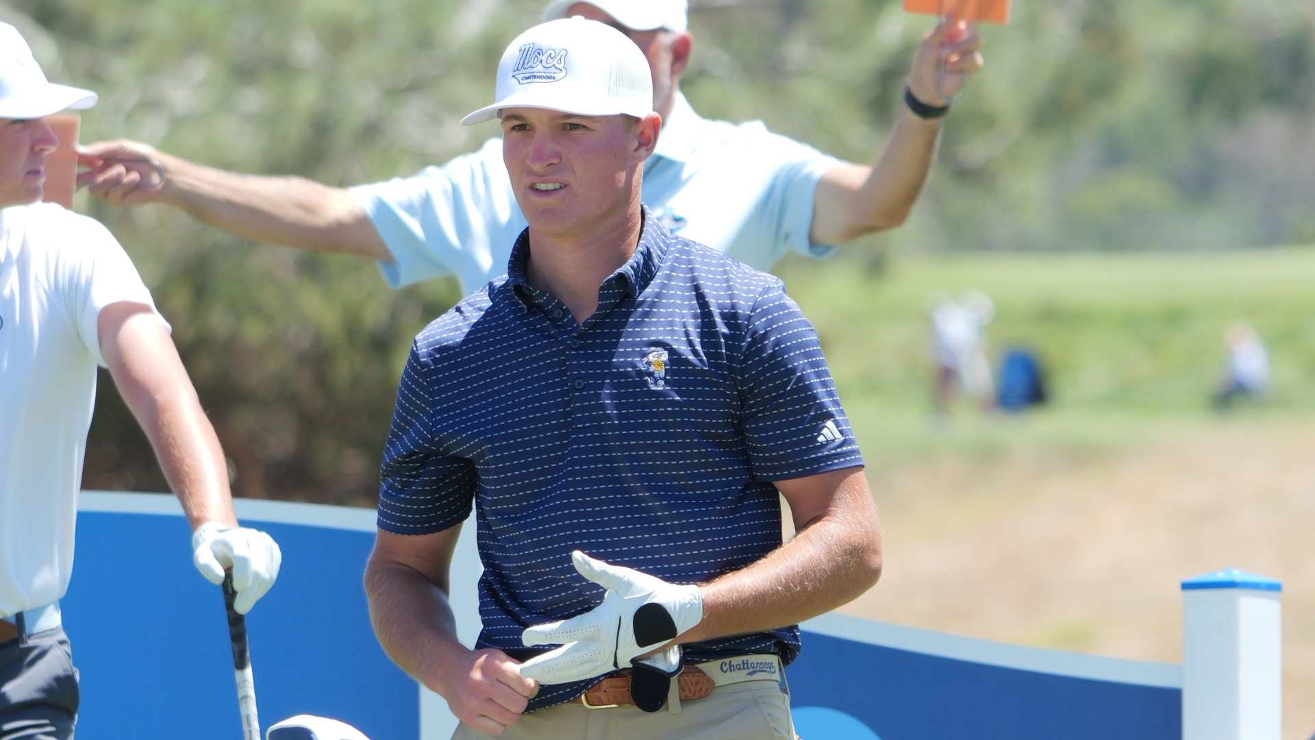 Griffin Law stares at his drive in the fairway from behind his bag at the tee as he adjusts his glove.