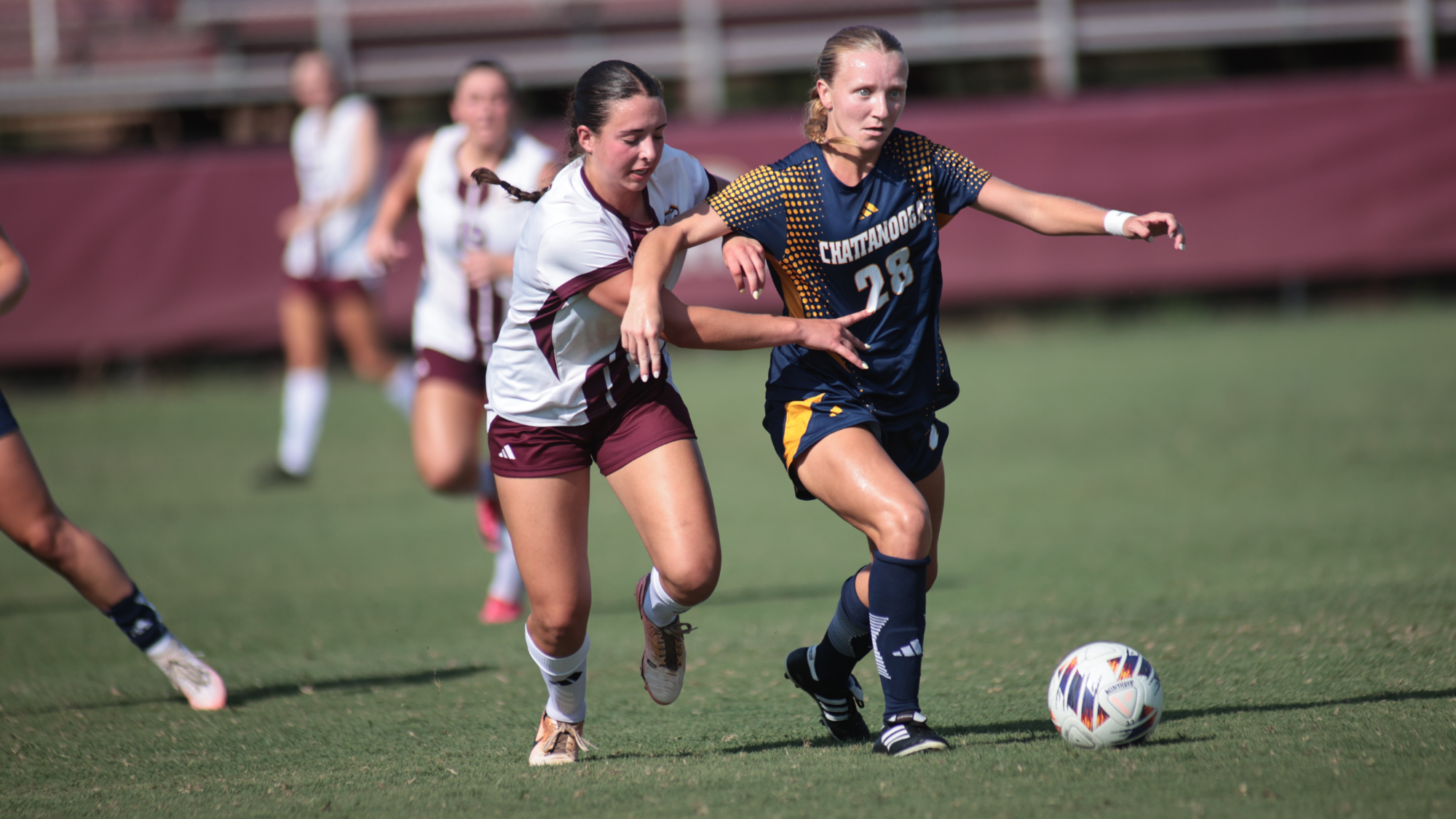 A soccer player with the ball is trying to separate herself from the defender.