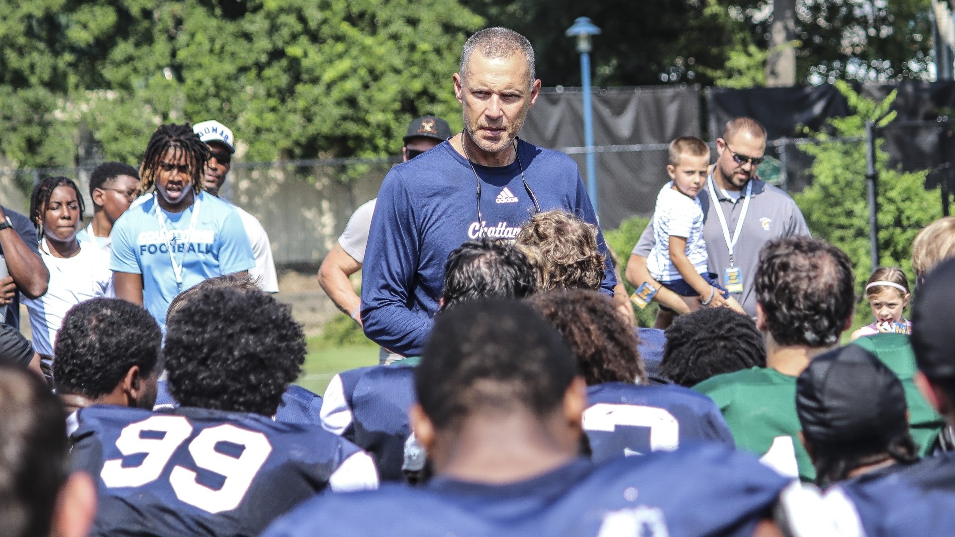 Coach Rusty Wright talks to the squad with alums and their families behind him at the annual alumni camp practice.