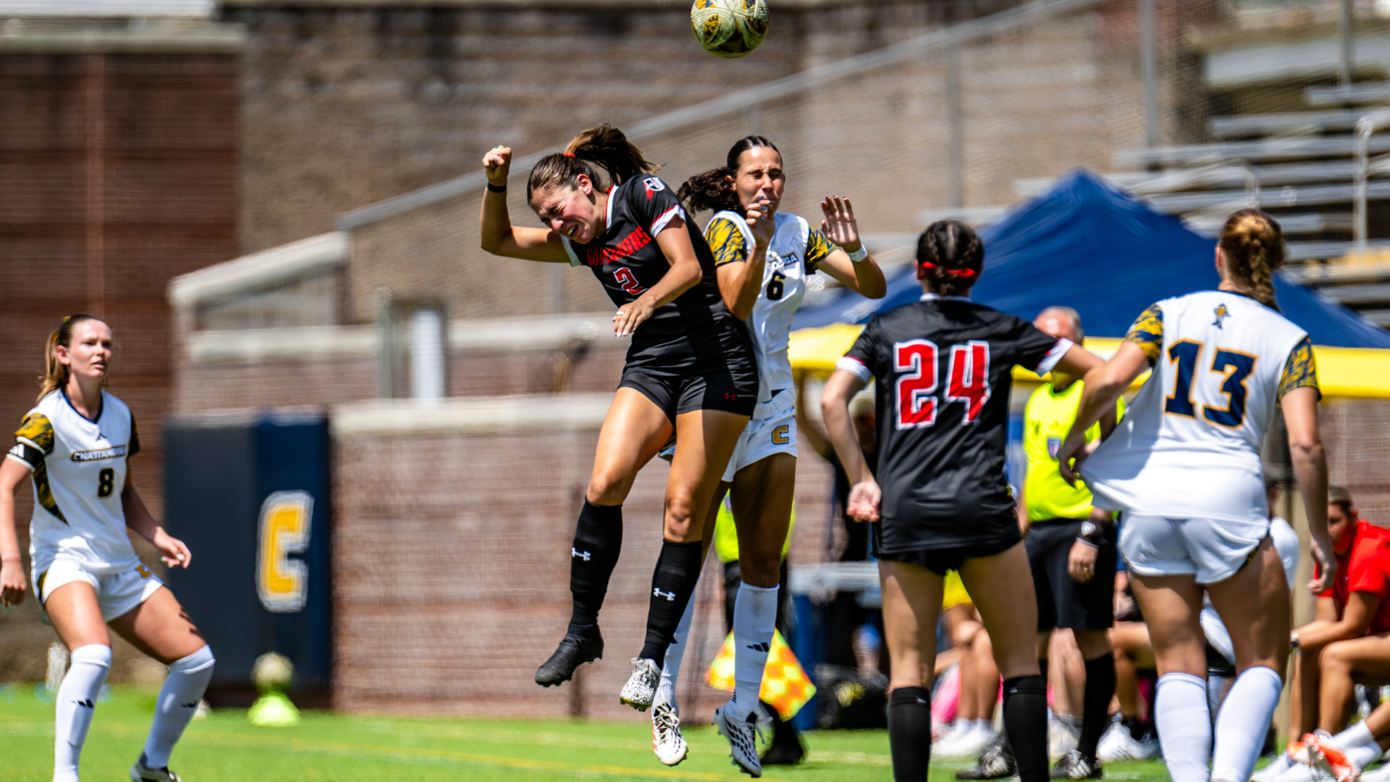 A soccer player in white and a soccer player in black both go up to head the ball during a game.