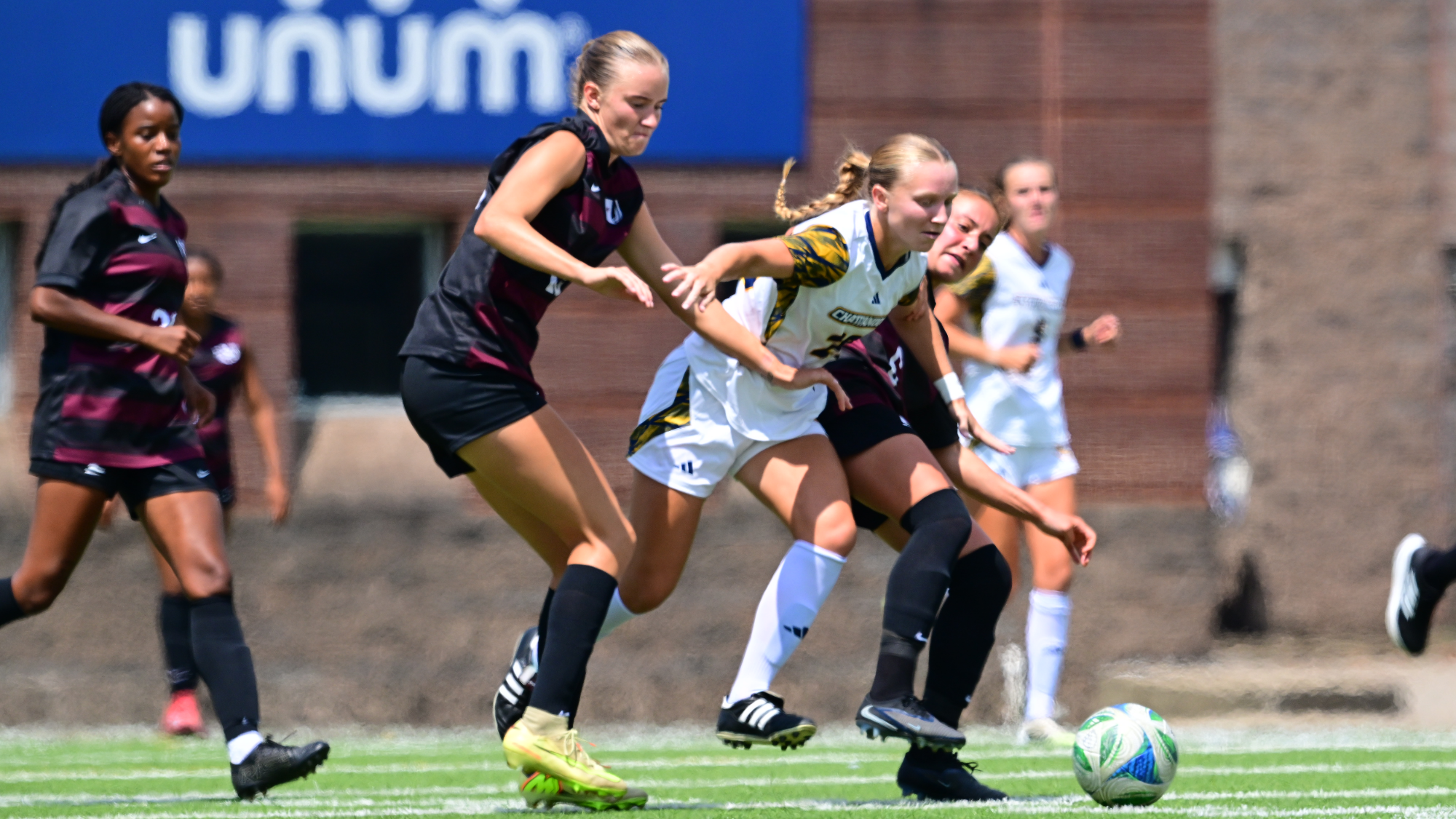 A soccer player in white and a soccer player in black are battling for the ball on the pitch.
