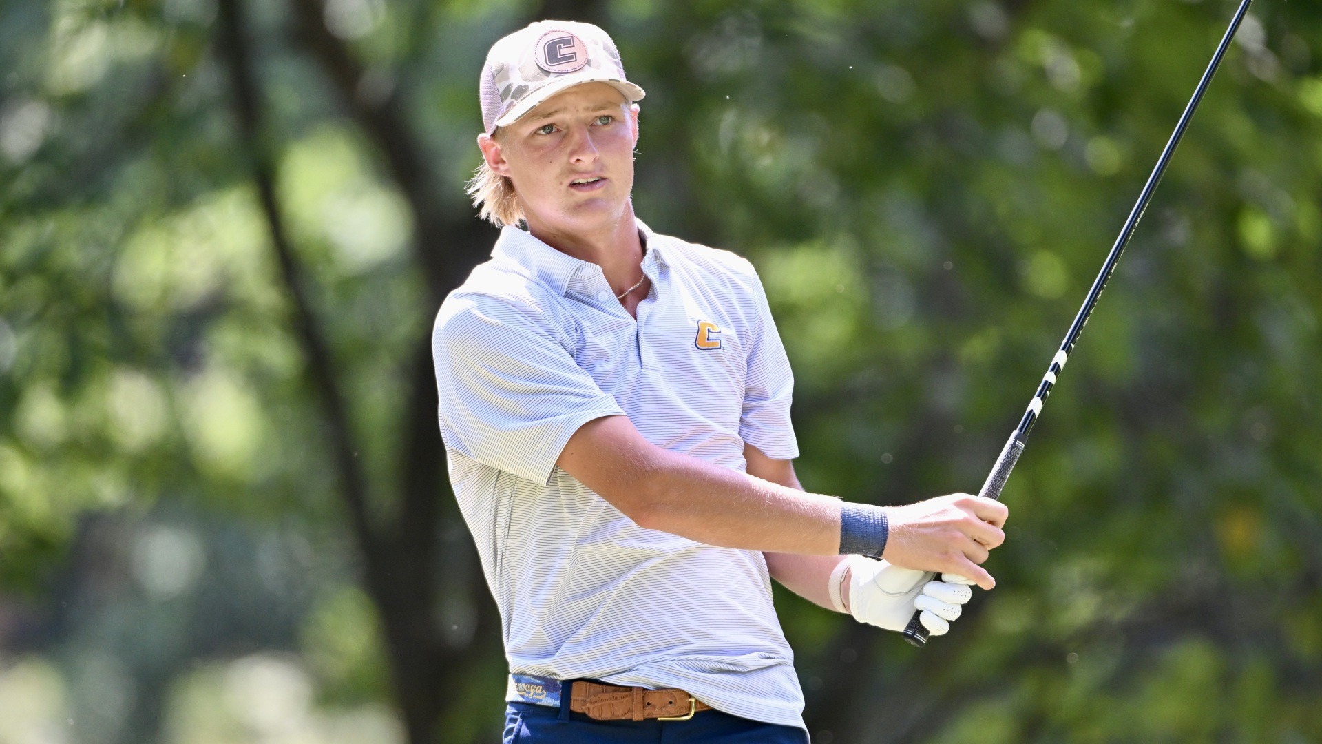 Evan Rogers follows his iron shot tracking the green with his hands in front, waist high, holding an upright club. 