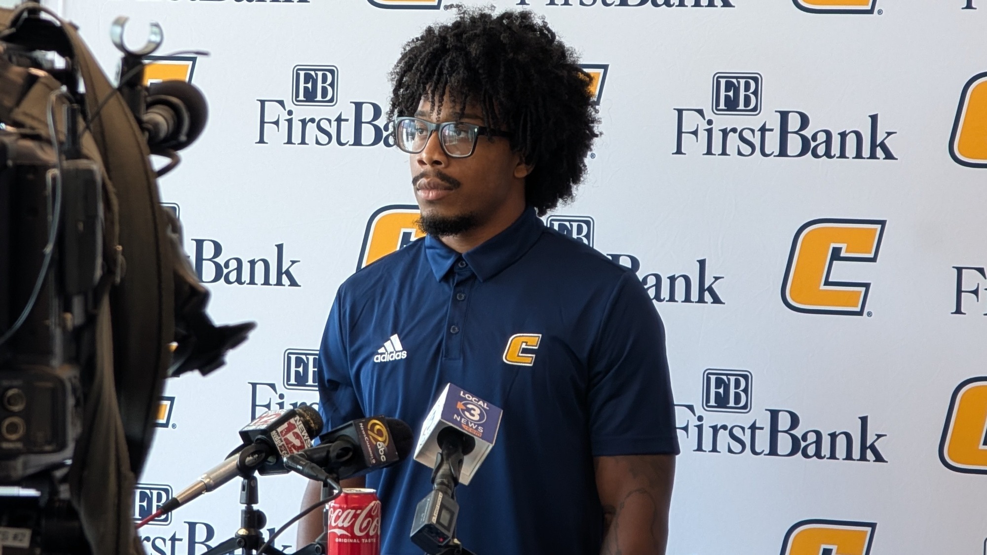 Kevin Lalin stands in front of the press conference backdrop with multiple TV microphones in front of him.