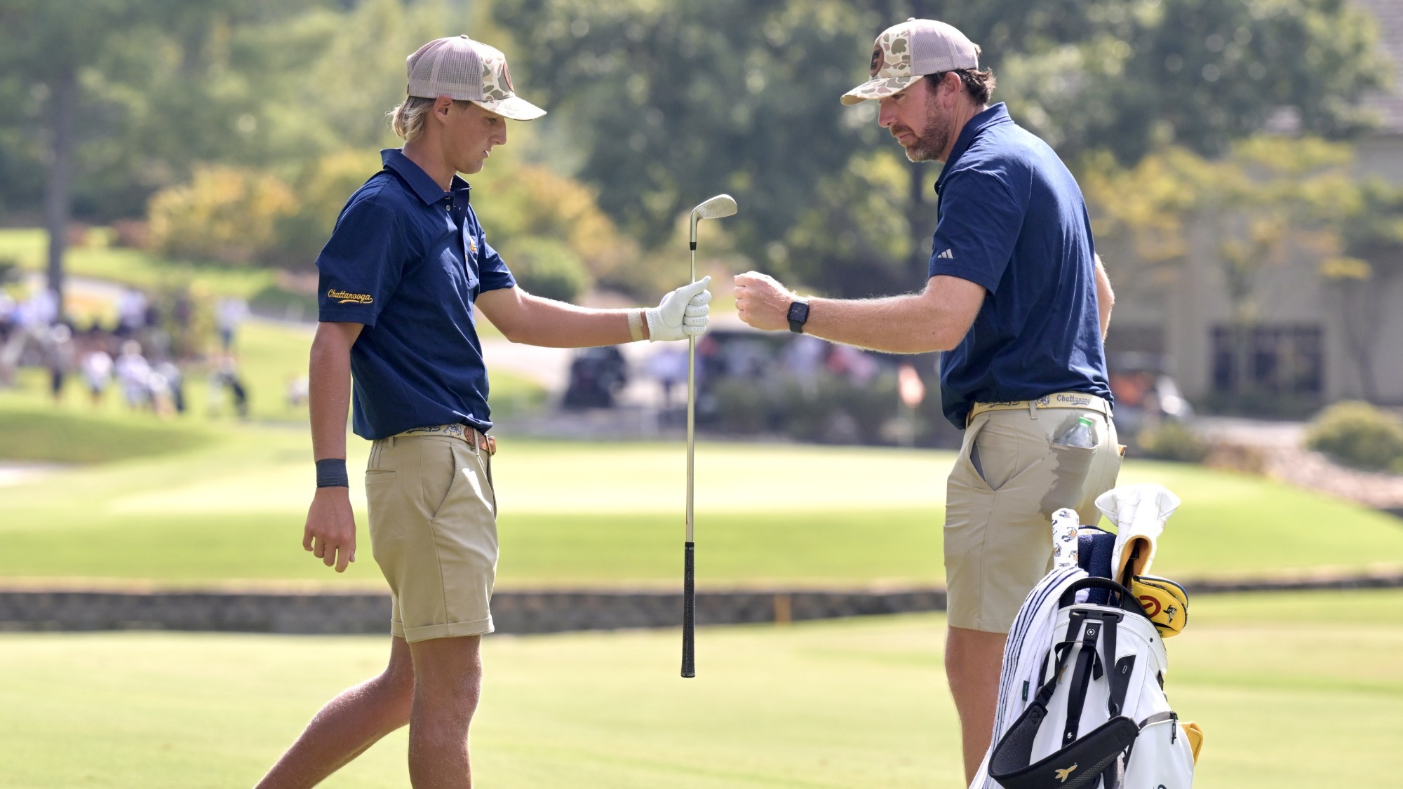 Evan Rogers with iron in hand and Coach Blaine Woodruff fist bump after a solid approach to the green in the background.