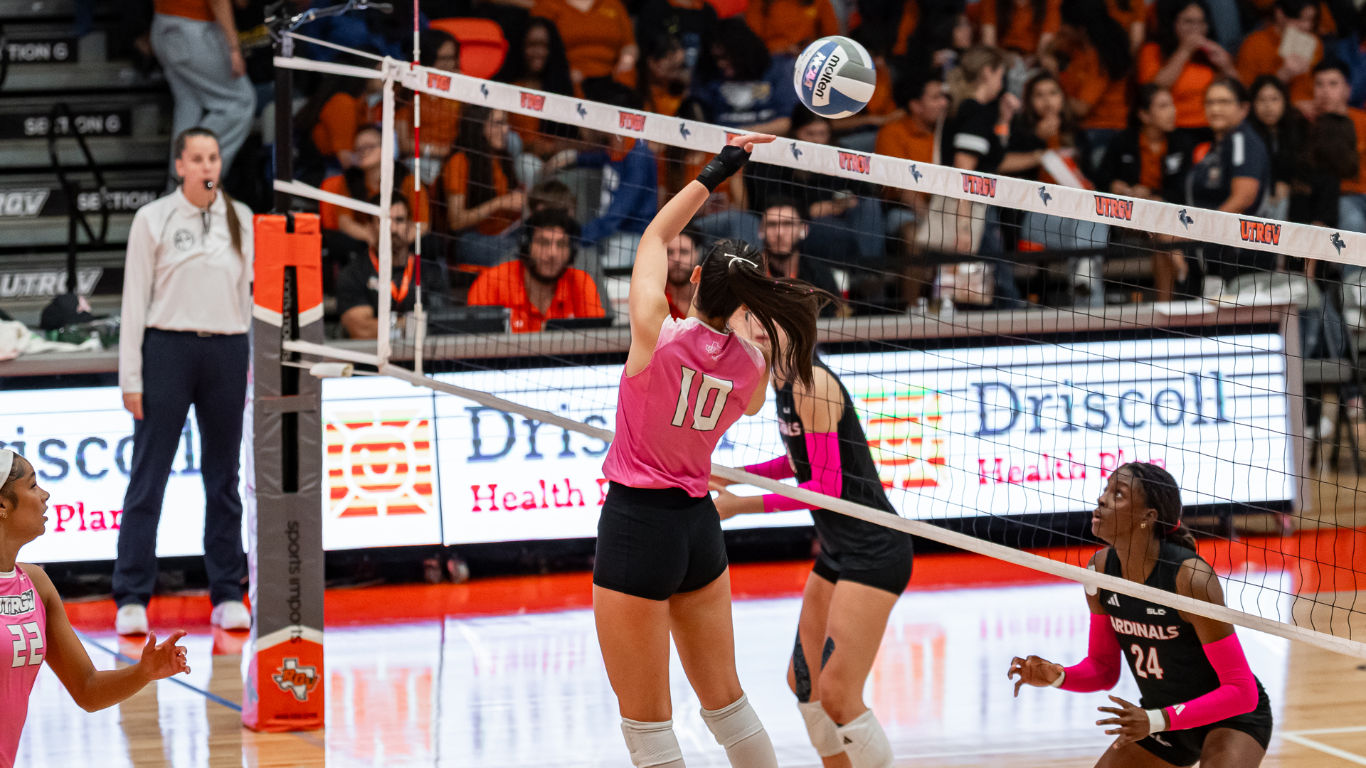 Image shows a volleyball player in a pink uniform wearing #10 attacking with a setter dump