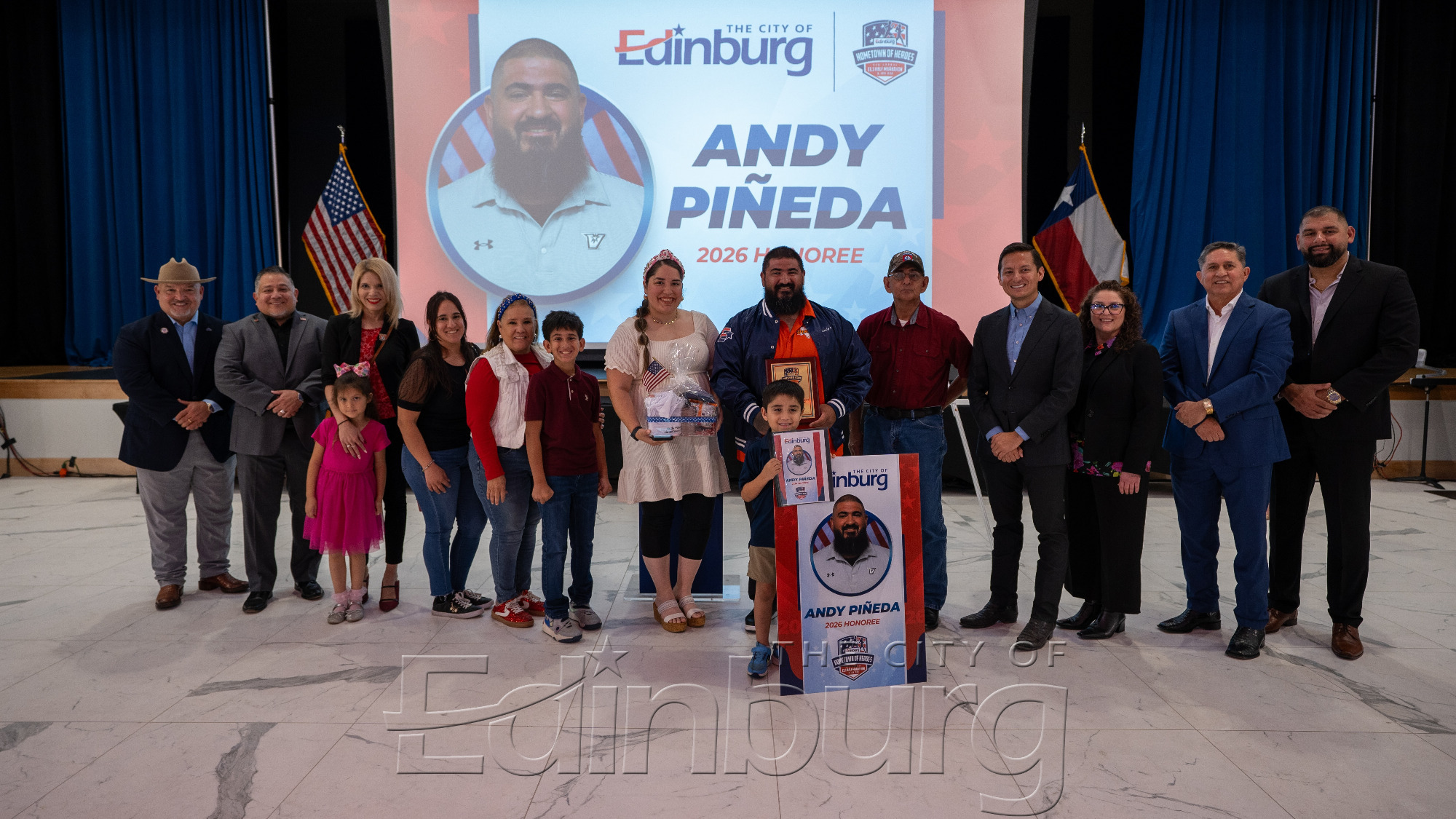 Andy Pineda, his family, and the Edinburg City Council posing in front of a graphic of Pineda being declared a City of Edinburg Hometown Hero