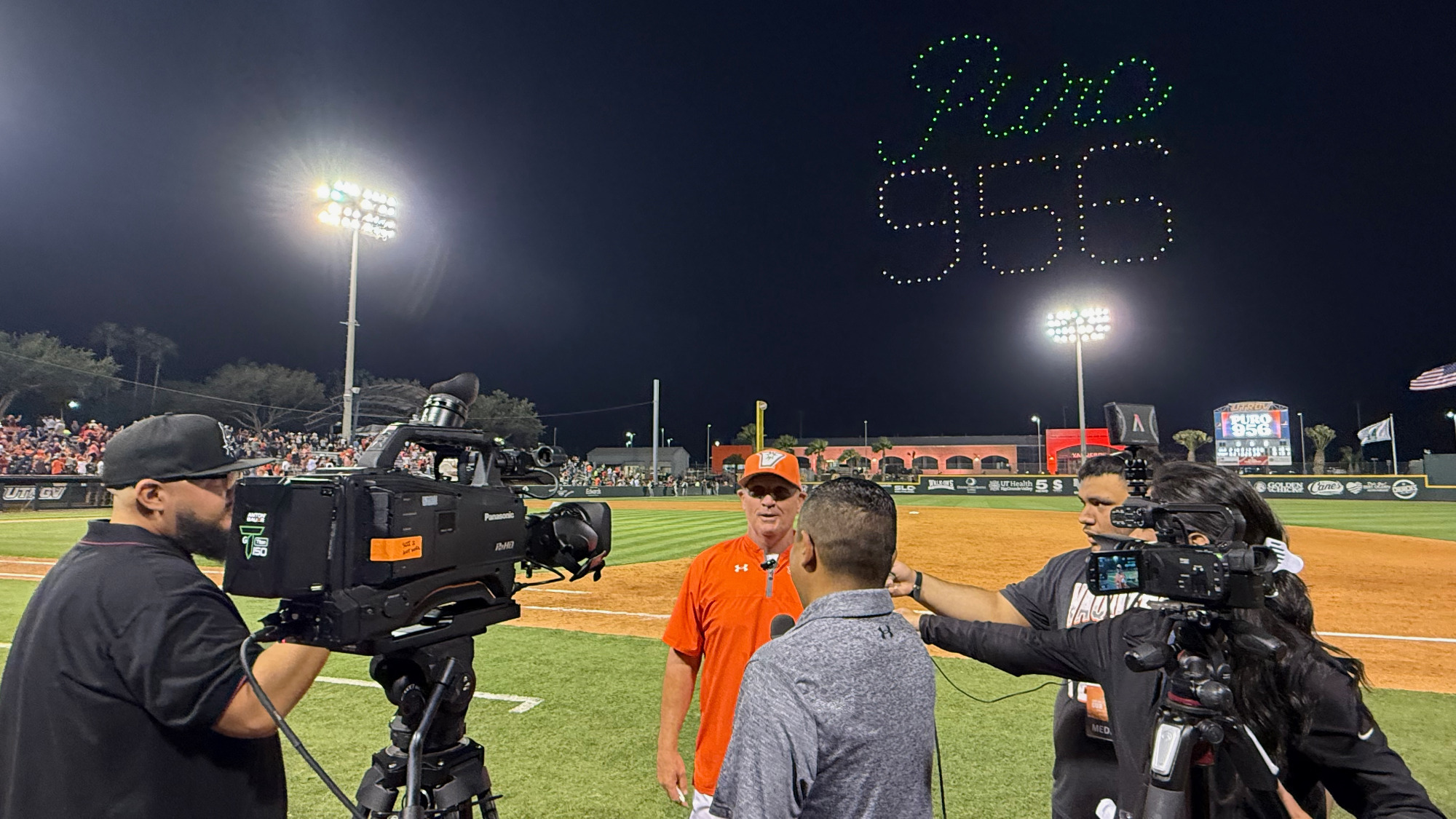 Coach Matlock speaking to the media while Puro 956 is spelled out in drones overhead