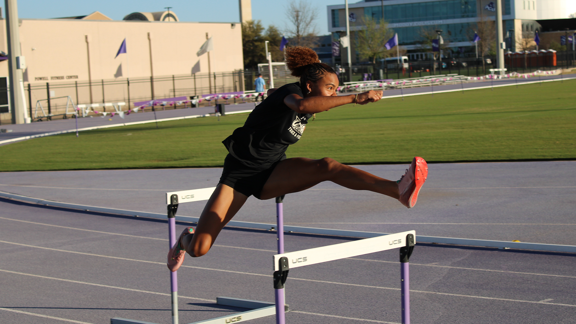 Photo of UTRGV track & field freshman Talyna Ligier in a black shirt and black tights jumping over a hurdle on the track during practice.