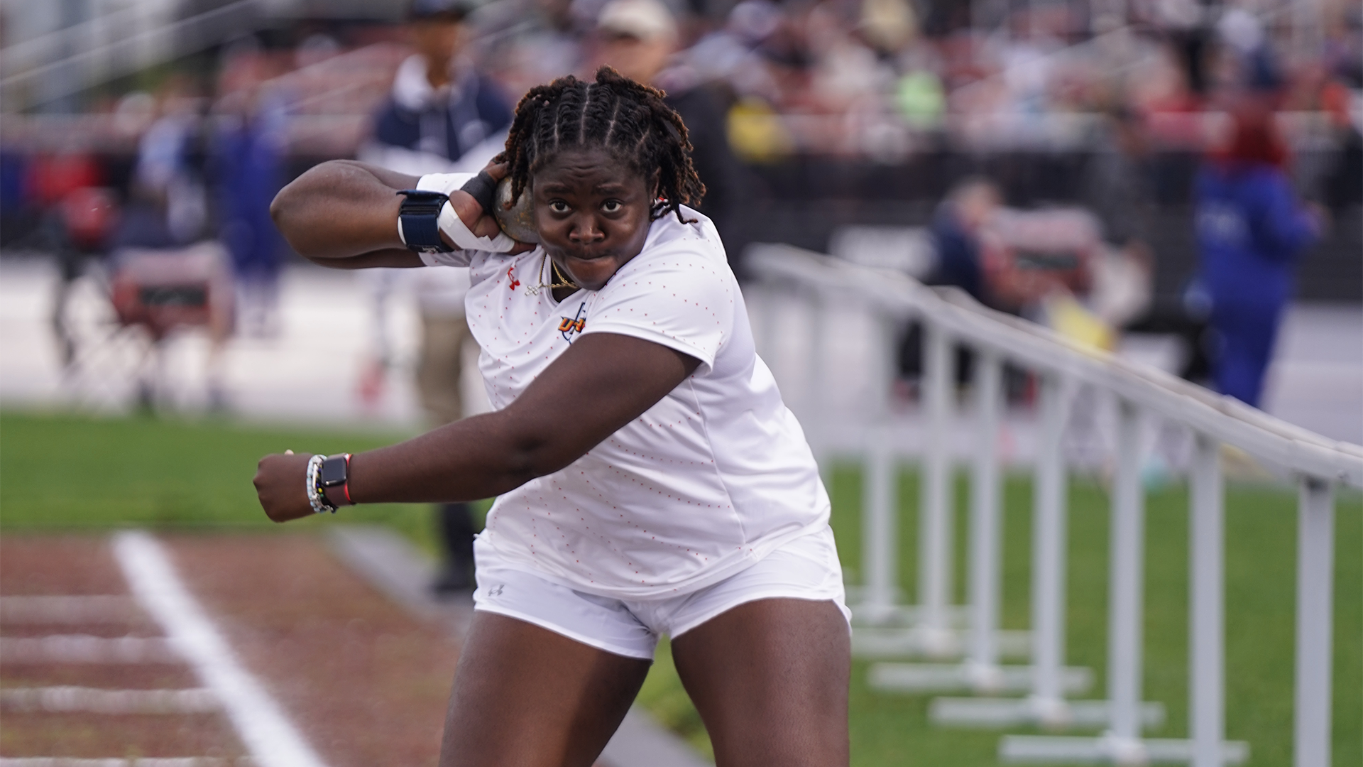 Image shows Efe Latham in a white UTRGV track & field uniform looking directly at the camera while holding a shot put as she's about to start her turn.