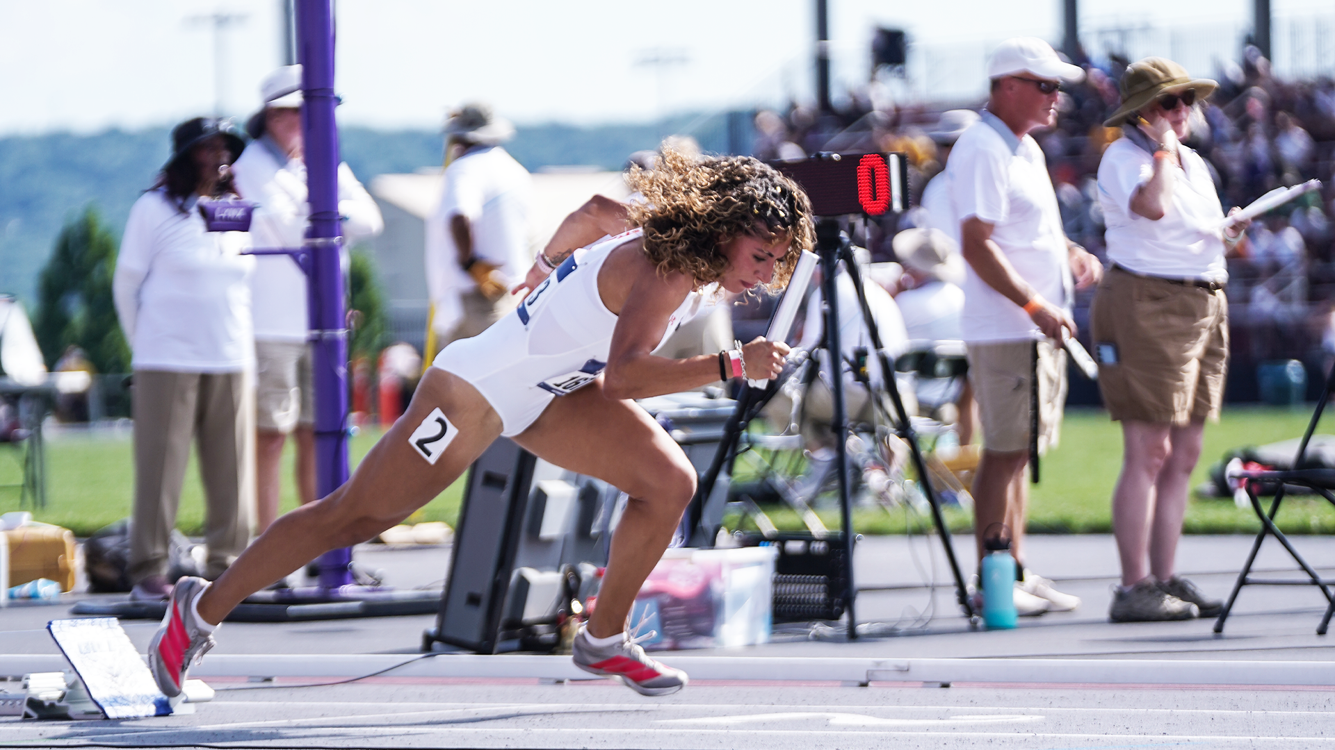 Image shows Ashley Lingueno in a white track uniform coming out of the blocks on the track at John McDonnell Field to start the 4x100-meter relay in the NCAA West First Round.