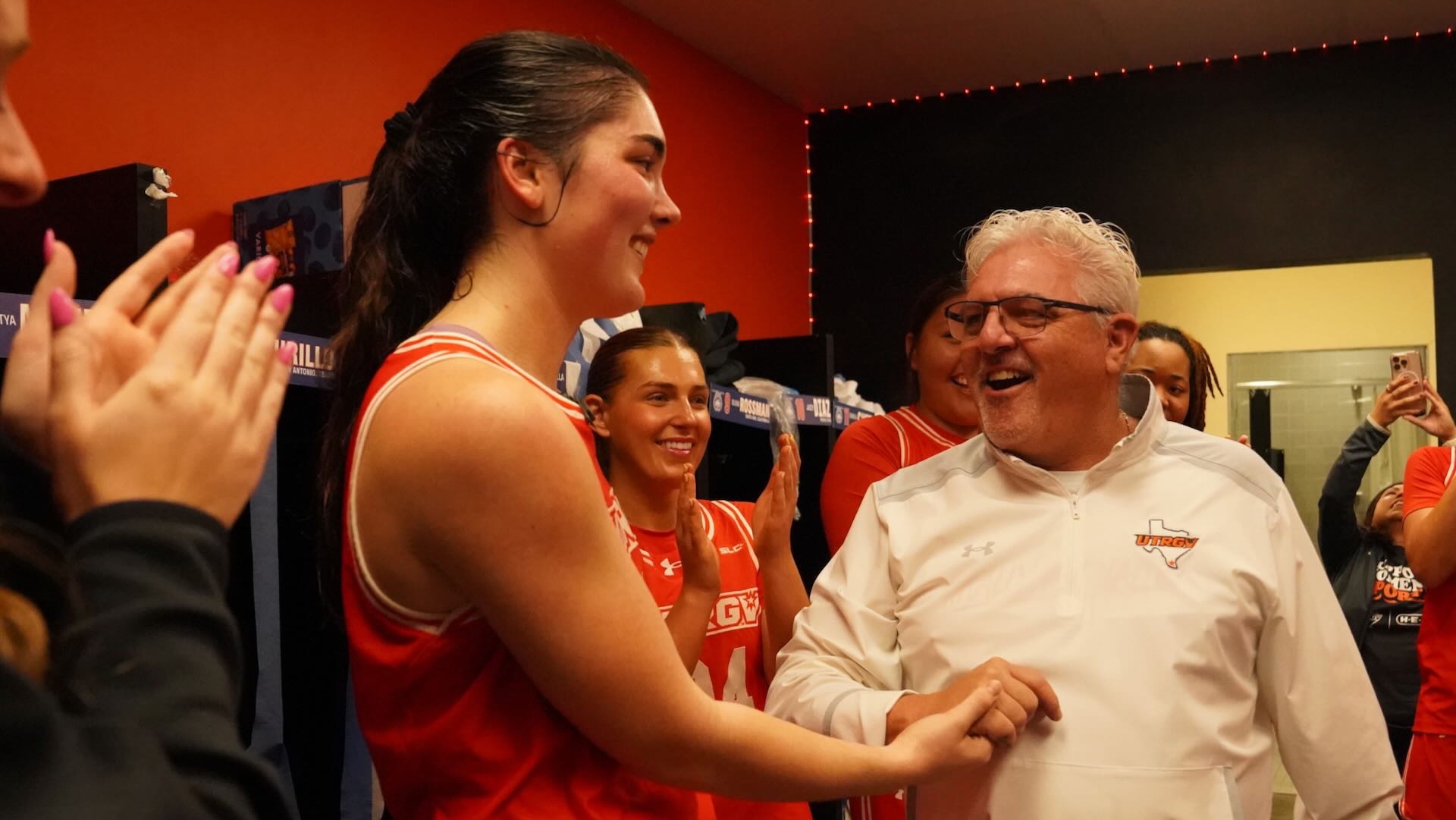 Photo of UTRGV WBB head coach Lane Lord smiling and shaking hands with Charlotte O'Keefe in the locker room after a win.