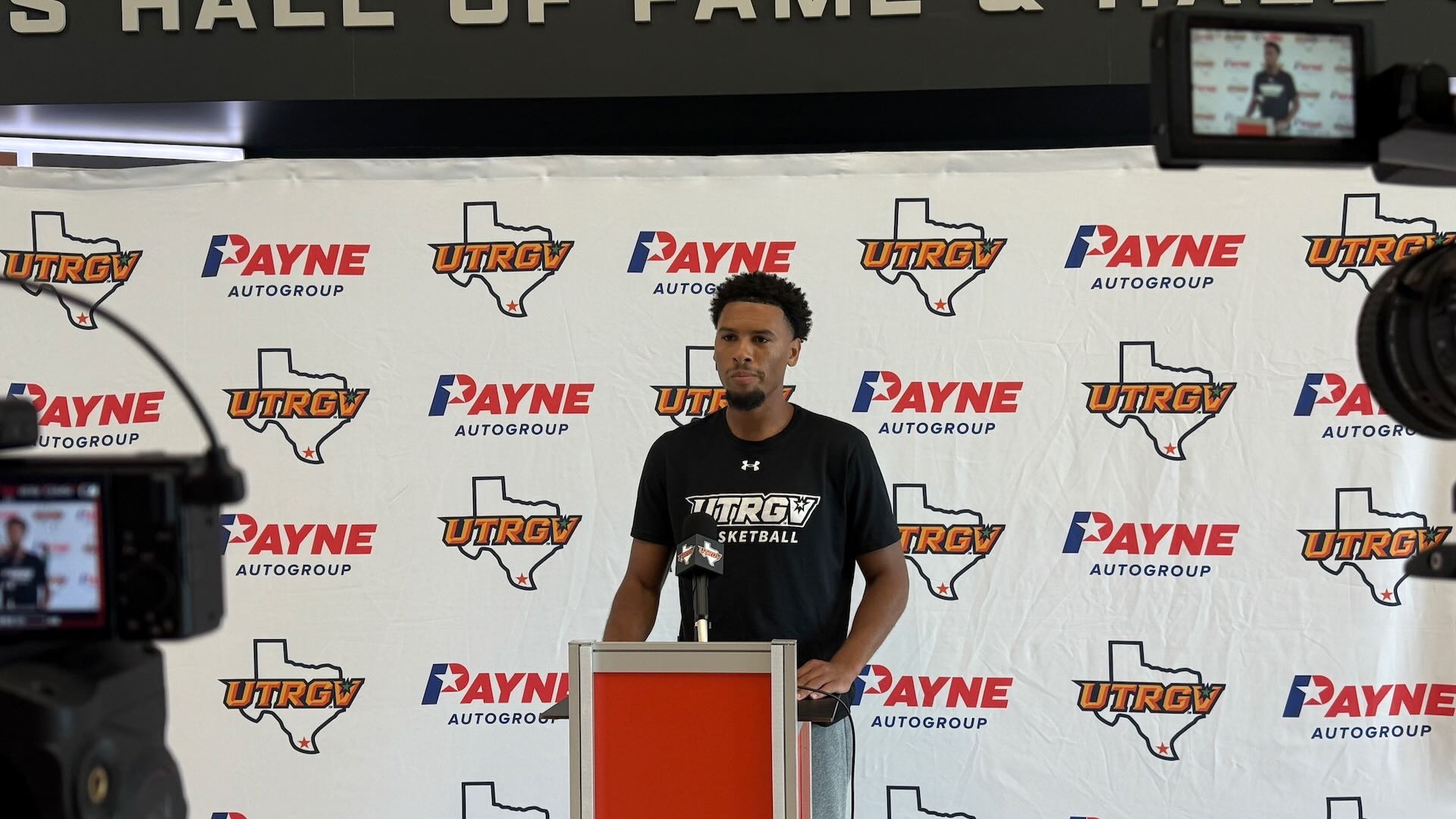 Image shows UTRGV men's basketball assistant coach Joseph Anderson standing at a podium in front of a white backdrop with UTRGV over Texas and Payne logos.