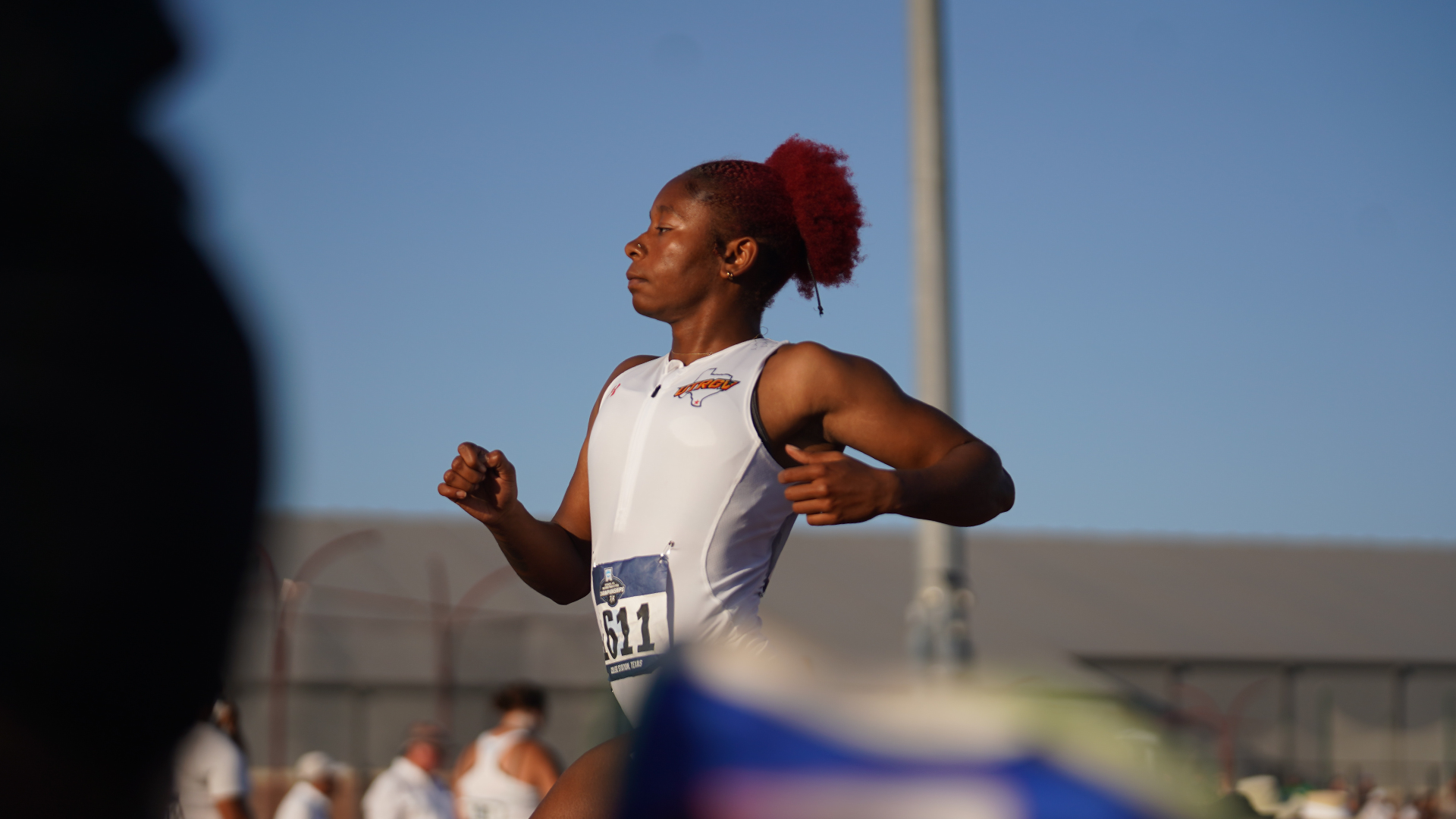 Image shows UTRGV track & field student-athlete Nayla Harris in a white speed suit crossing the finish line of a race.