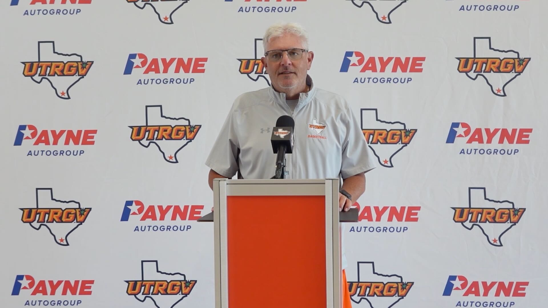 Lane Lord stands at a podium in front of a white backdrop with the UTRGV over Texas logo and the Payne Auto Group logo.