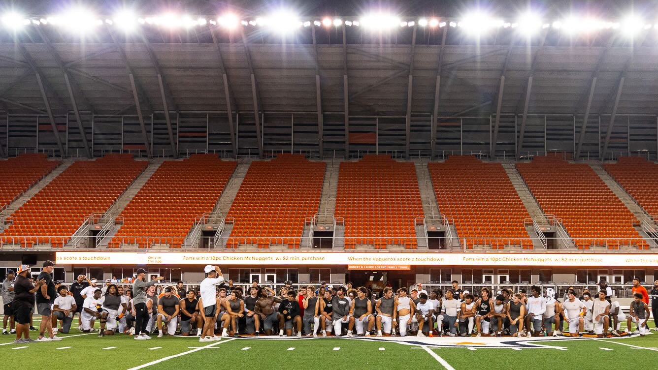 Image shows the UTRGV football team taking a knee listening to head coach Travis Bush at Robert and Janet Vackar Stadium.